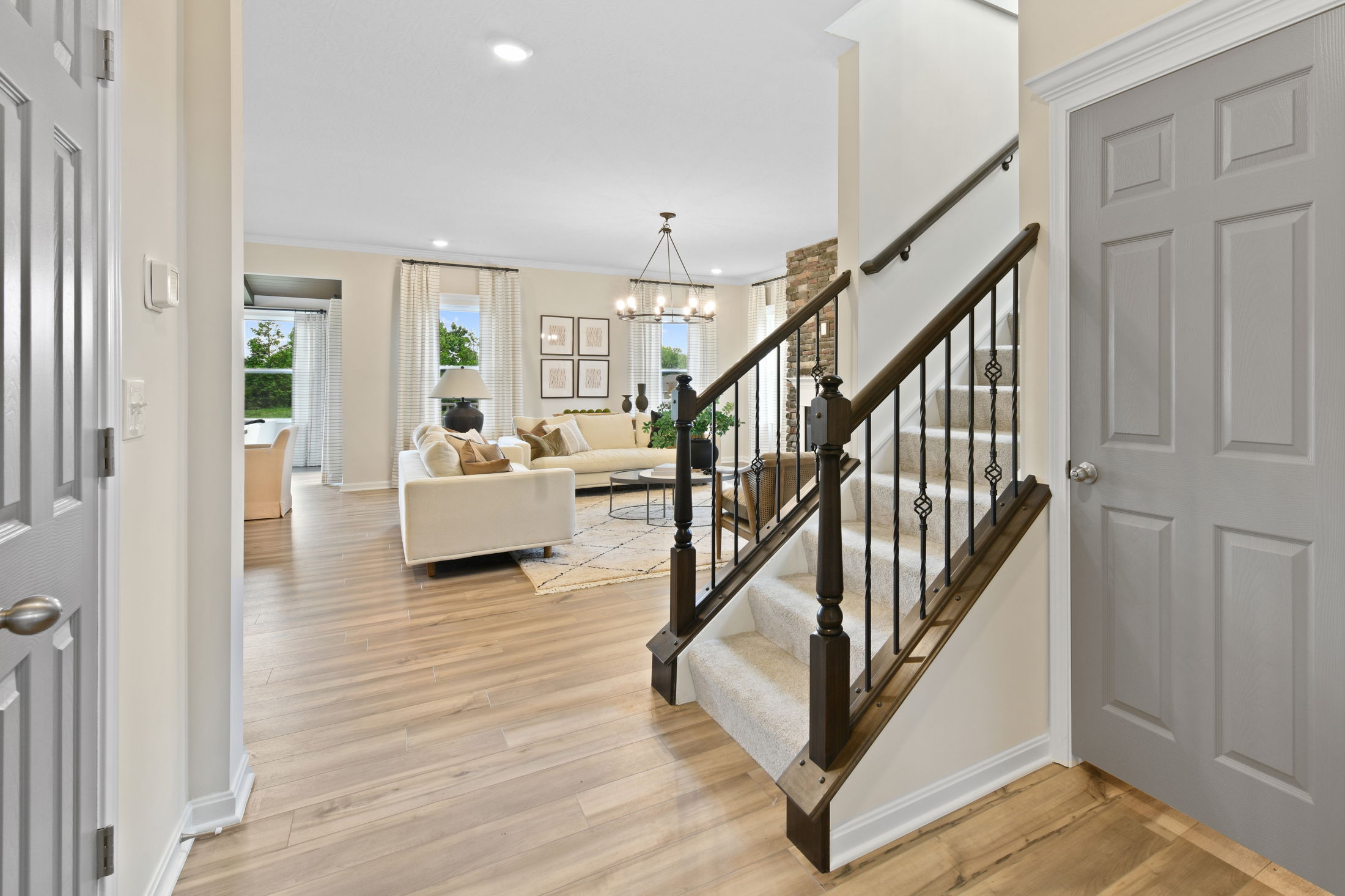 Modern living room with hardwood floors, elegant staircase, and neutral furnishings.