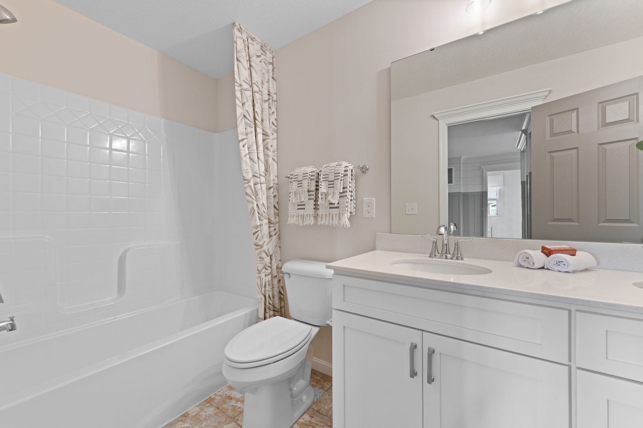 Modern bathroom with white vanity, large mirror, and shower-tub combo featuring a patterned curtain.