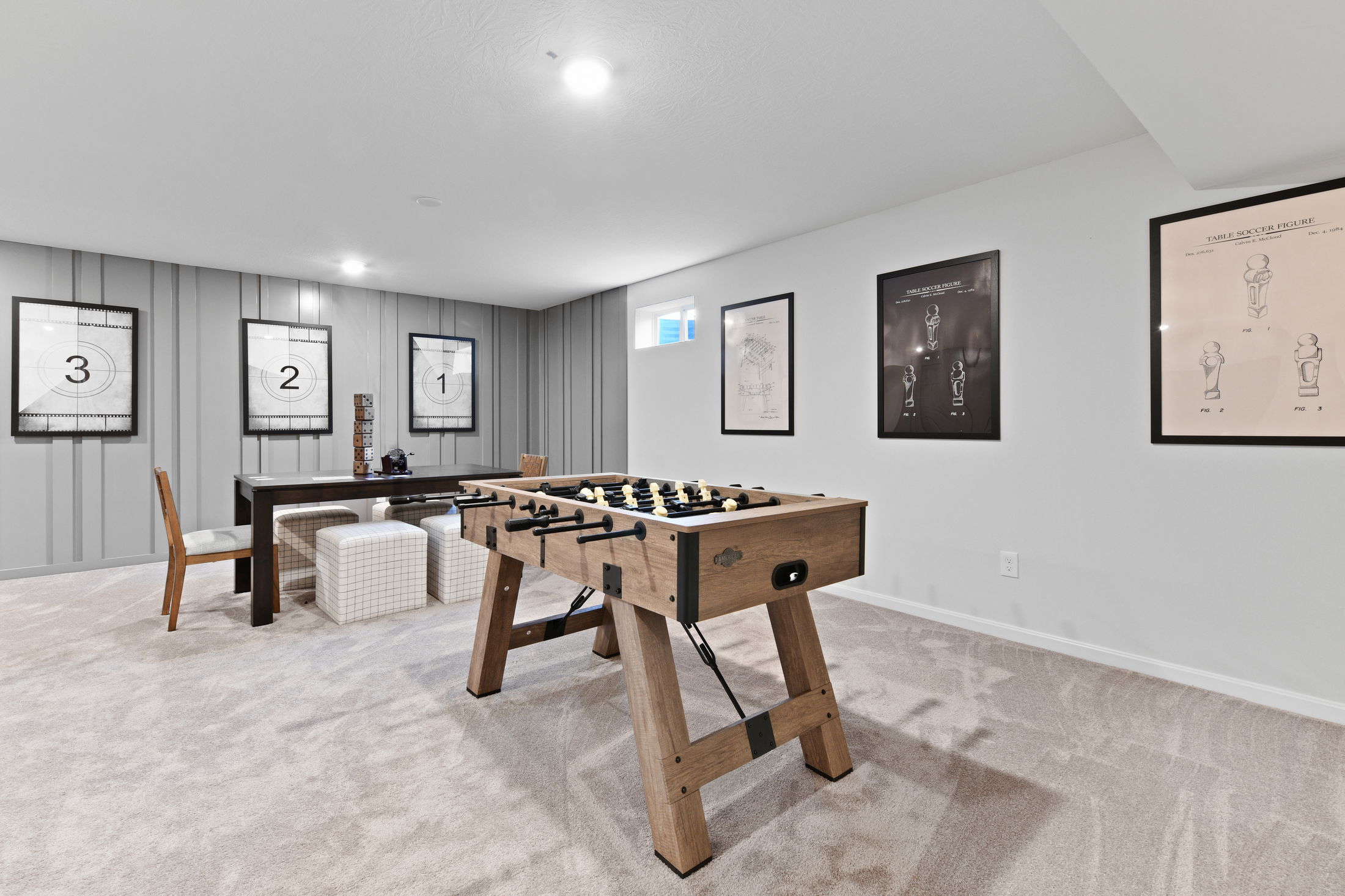 Modern basement game room with a wooden foosball table, neutral decor, and framed wall art.