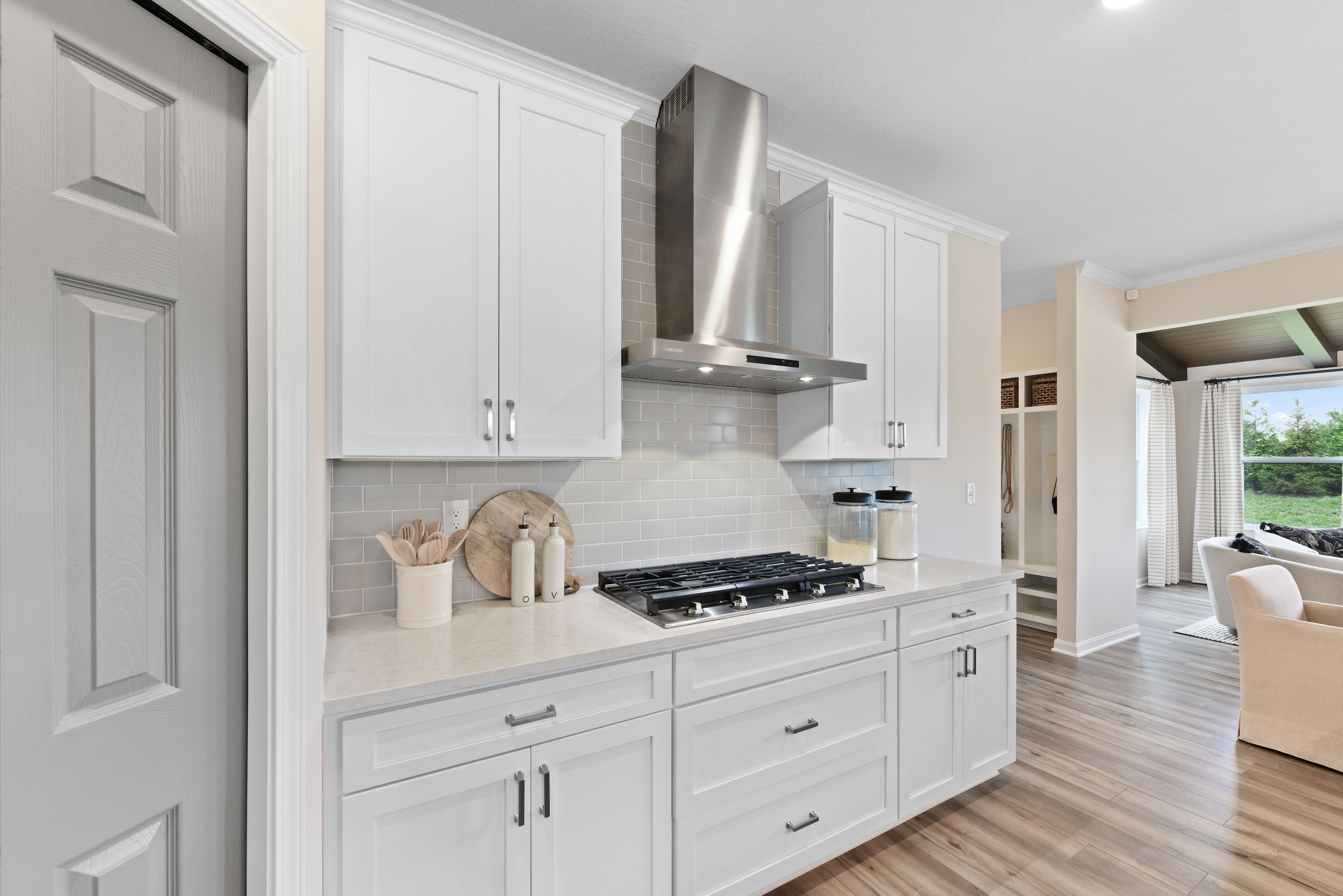 Modern kitchen featuring white cabinets, stainless steel range hood, and a gas stovetop, with light wood flooring.