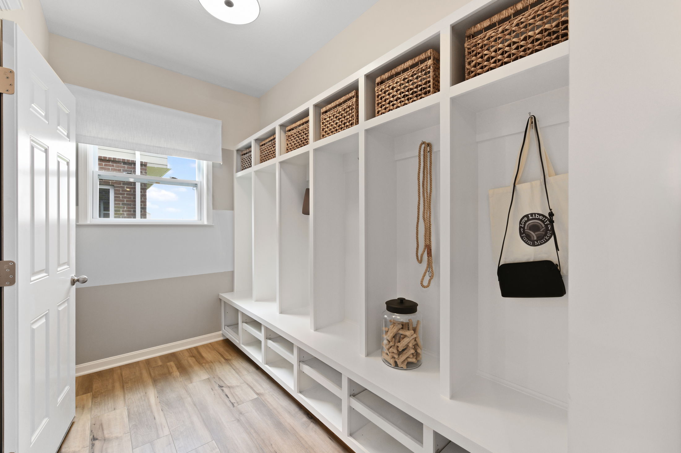A bright and spacious mudroom with built-in white cubbies, wicker baskets, and a window letting in natural light.