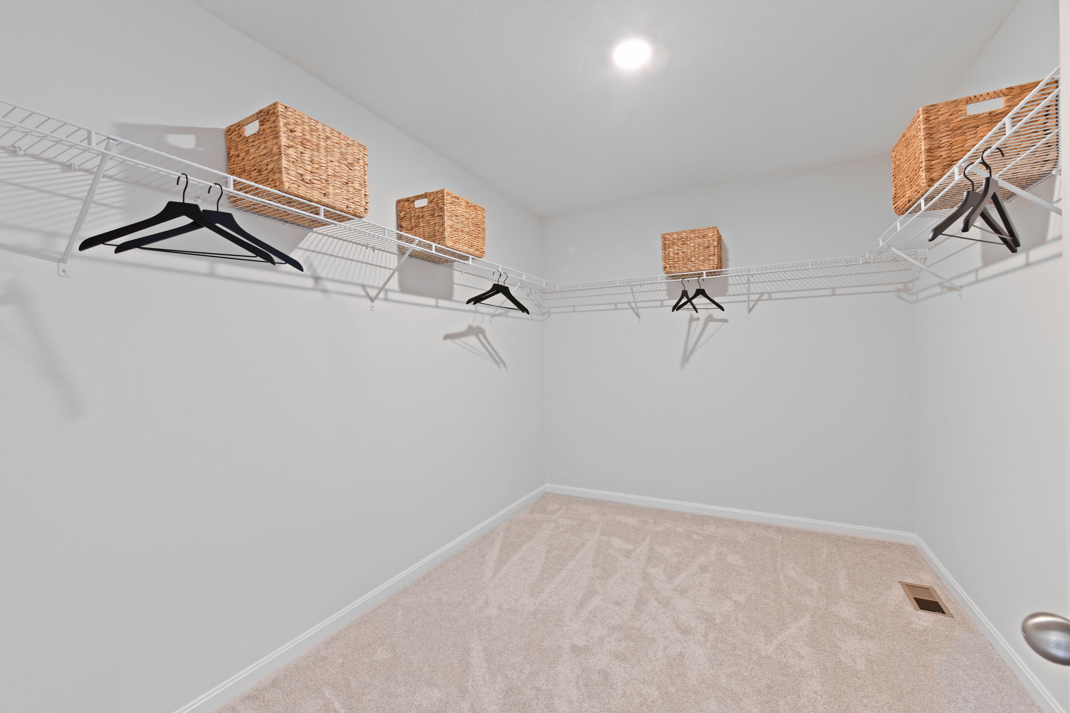 Spacious walk-in closet with white wire shelving, black hangers, and woven storage baskets on beige carpeting.