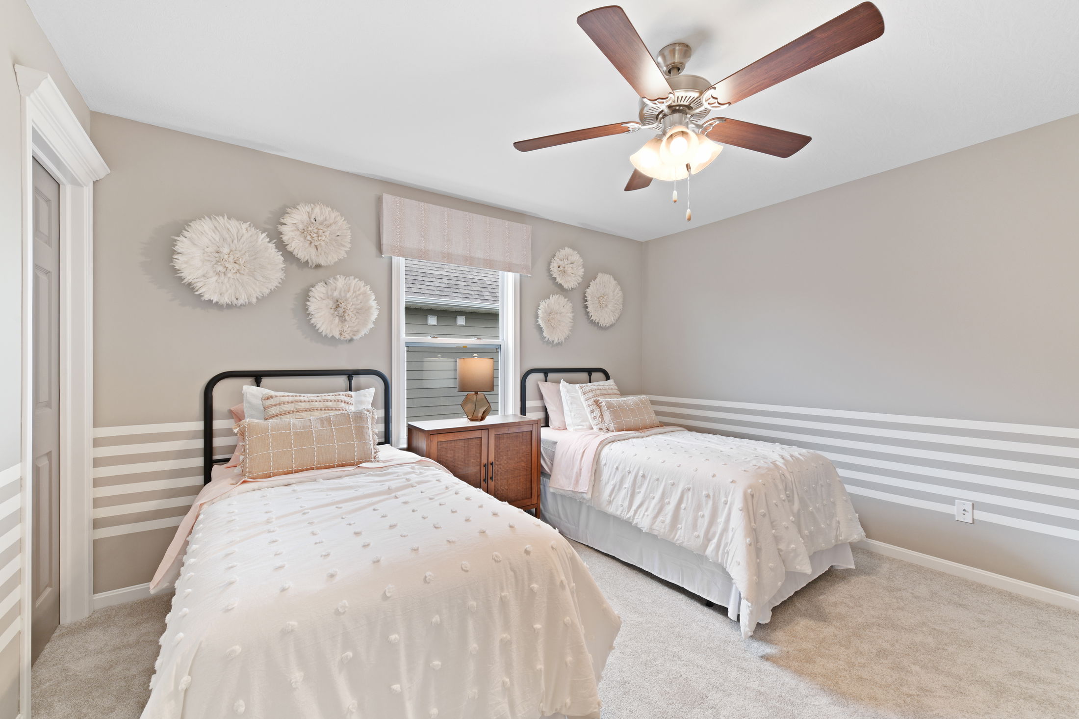 Twin beds with white bedding and decorative pillows in a stylishly decorated bedroom featuring wall art and a ceiling fan.