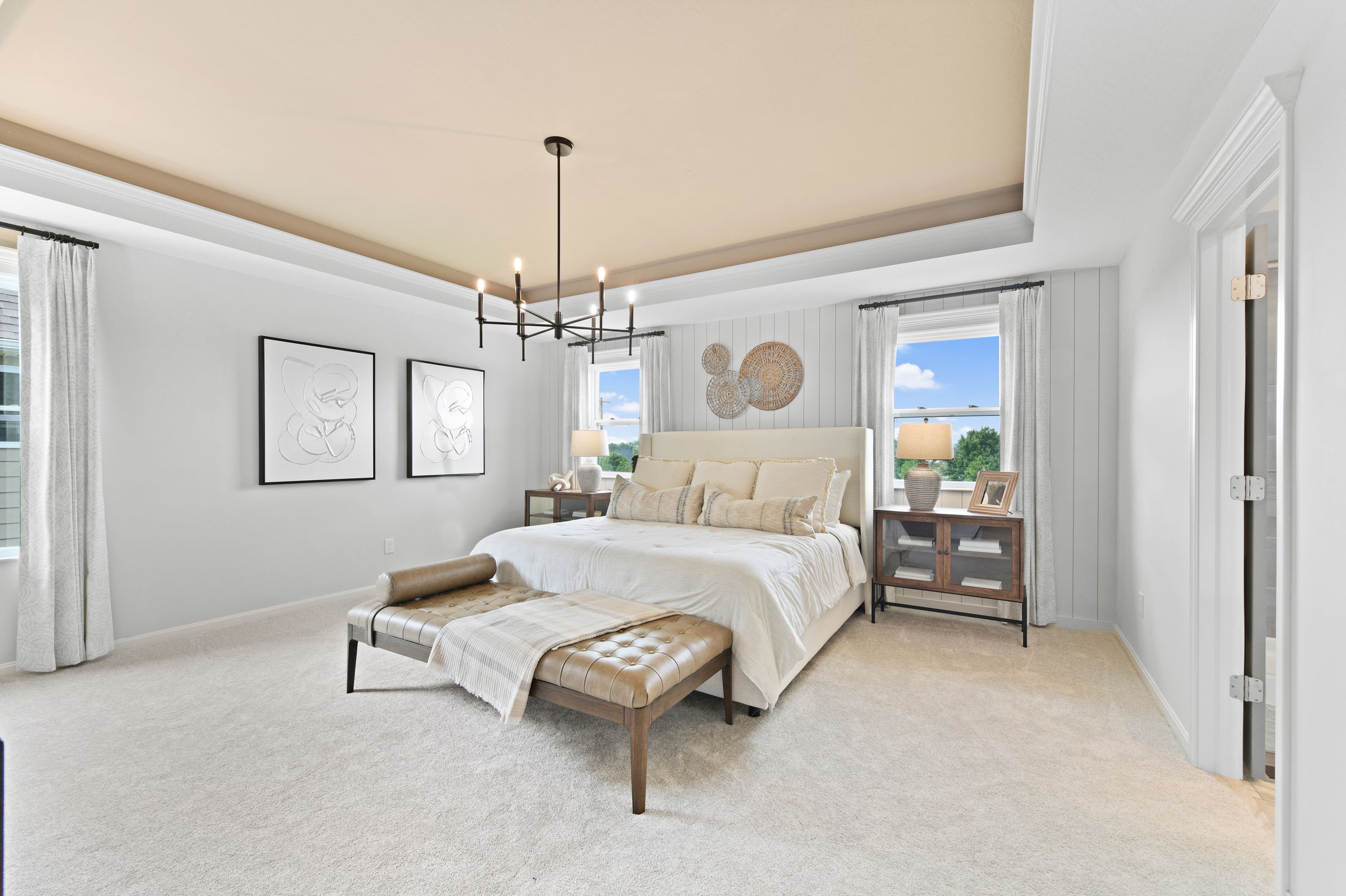 Luxurious modern bedroom with neutral tones featuring a stylish bed, elegant chandelier, and artwork on the walls.