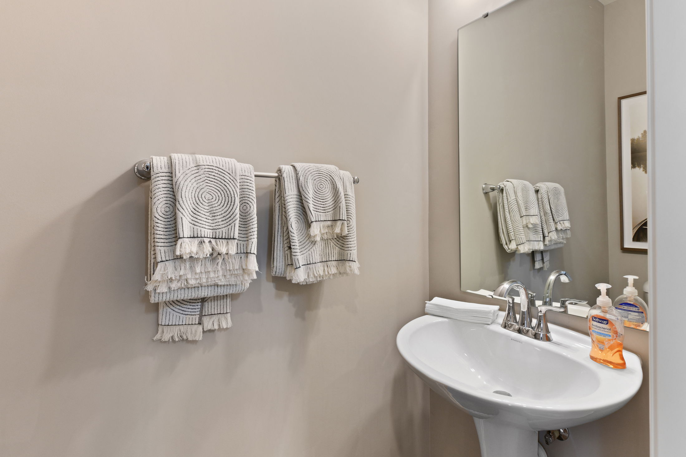 Elegant bathroom with pedestal sink, decorative towels, and a mirror reflecting a stylish, contemporary design.
