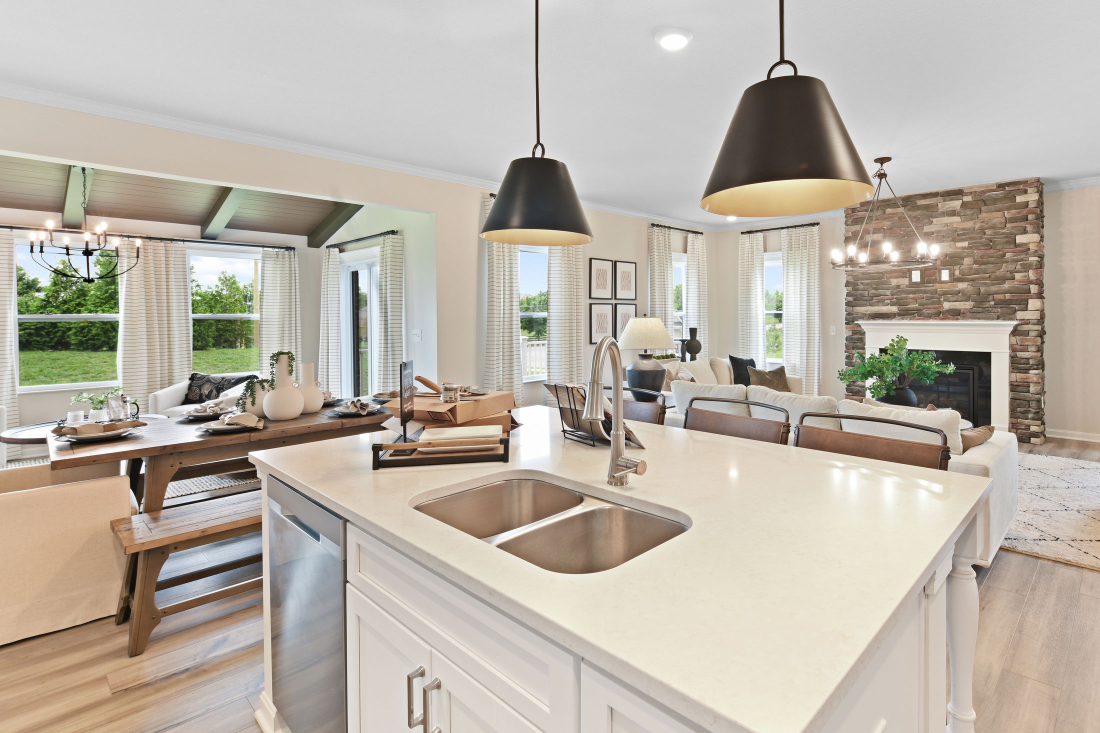 Luxurious open-concept living and dining area with modern lighting, a stone fireplace, and large windows.