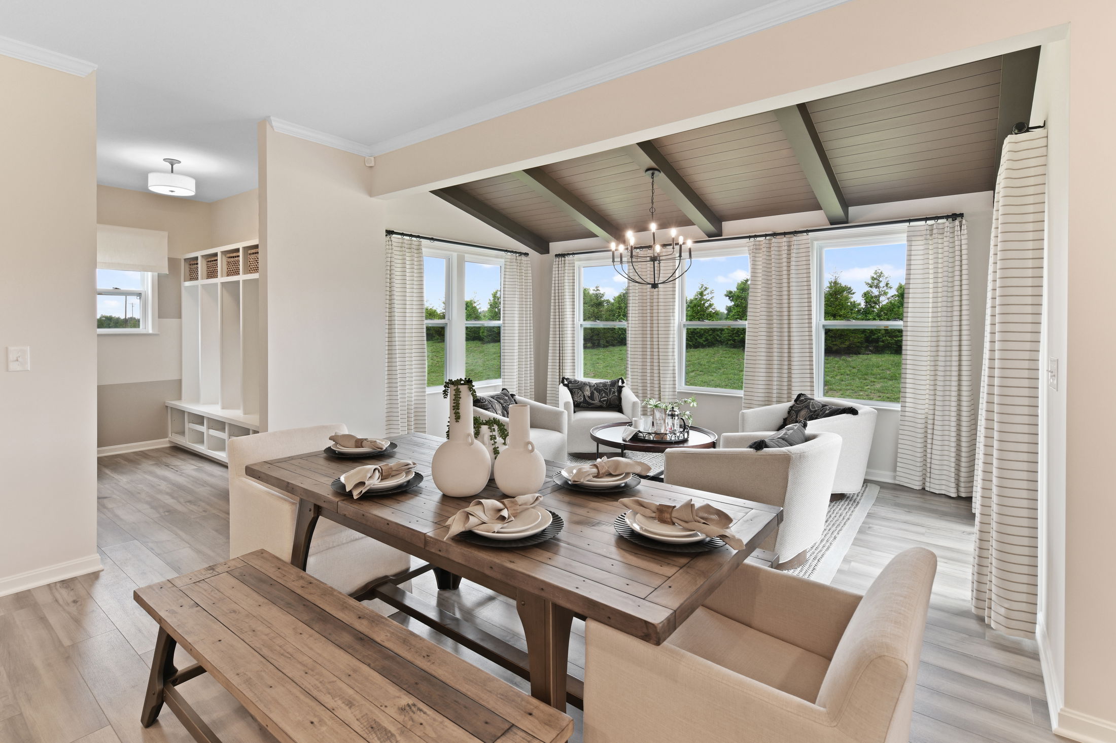 Bright and modern dining and living room area with wooden table, cozy seating, and large windows overlooking a green lawn.