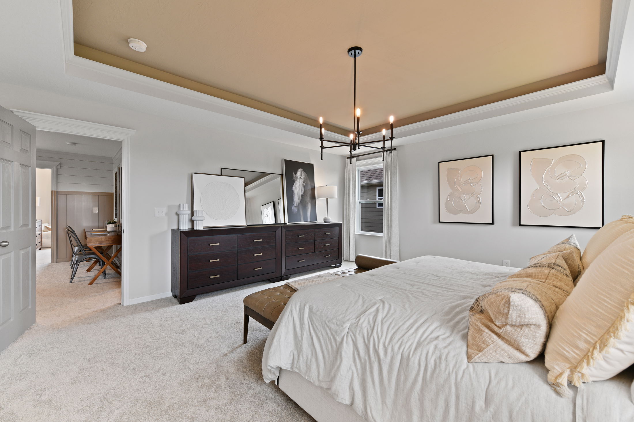 Modern bedroom interior with a stylish chandelier, art on the walls, and a dark wooden dresser.