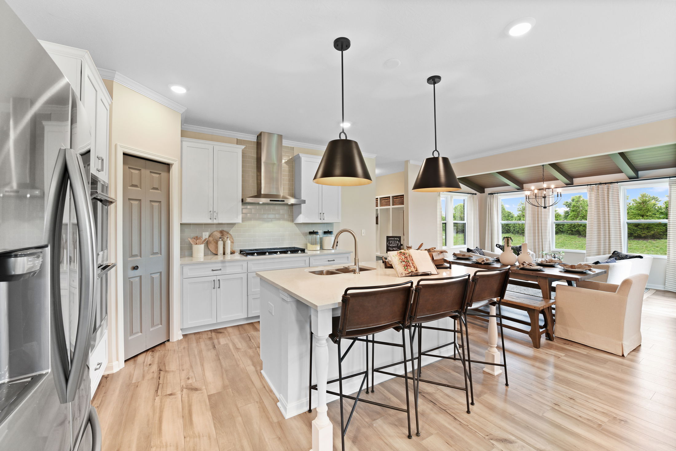 Modern open-plan kitchen and dining area with white cabinets, stainless steel appliances, and large windows providing natural light.