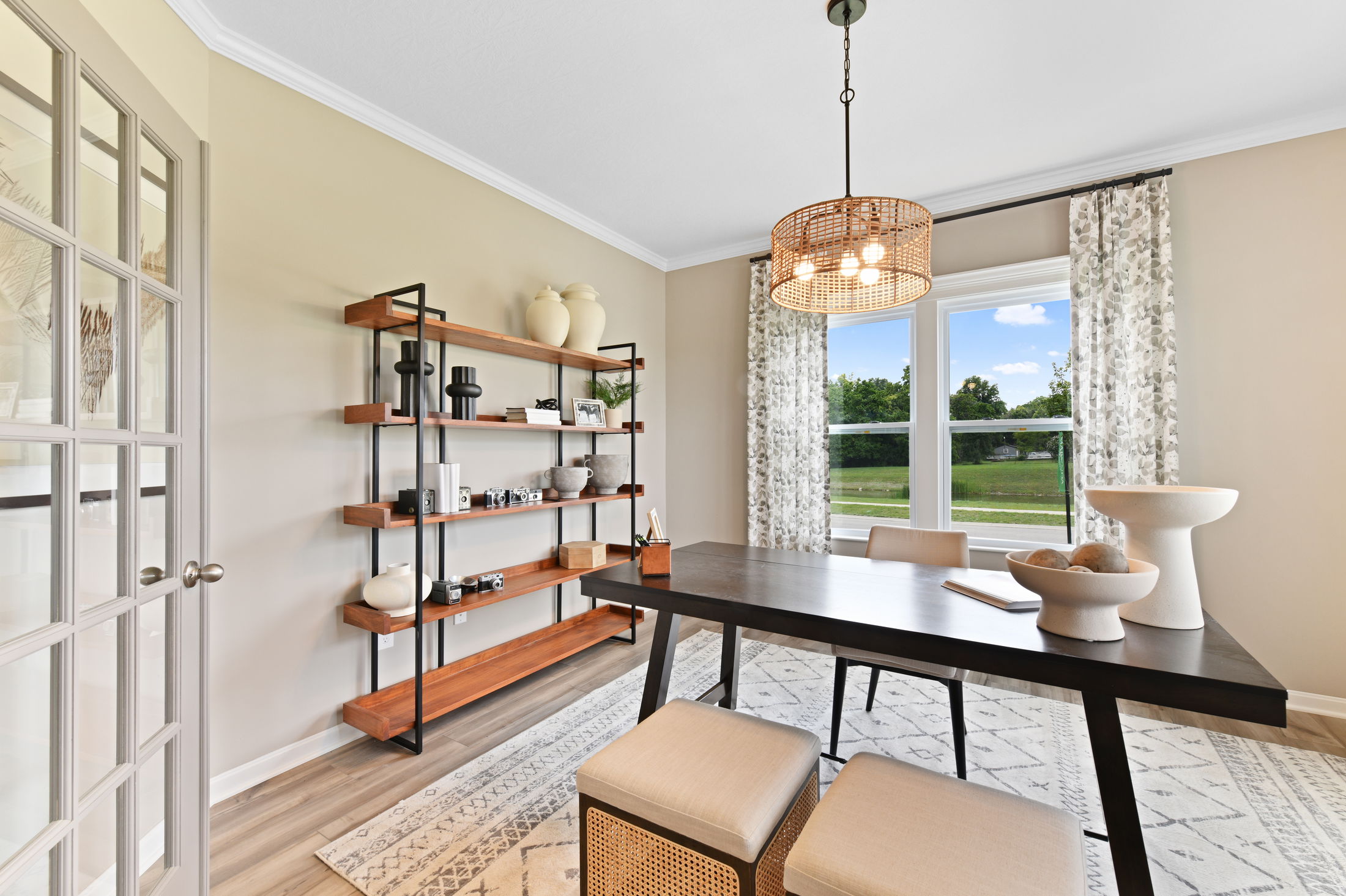 Stylish dining room interior featuring a modern wooden table, minimalist decor on shelves, and large windows with patterned curtains.