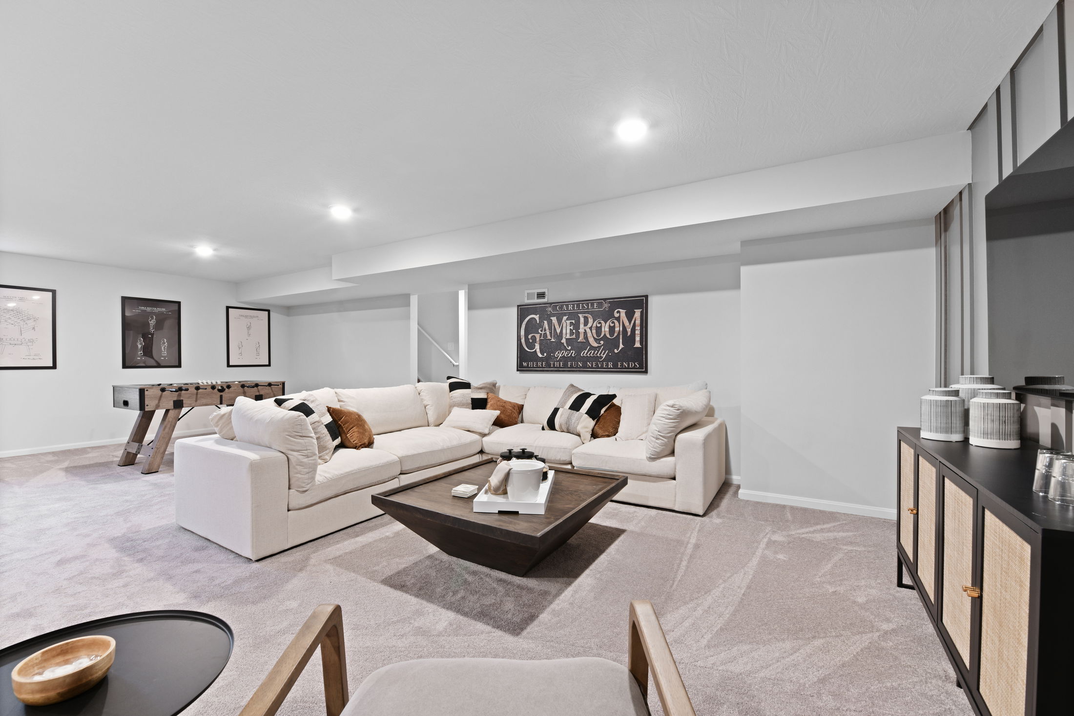 Stylish basement game room with comfortable sectional sofa, wooden foosball table, and modern decor accents.