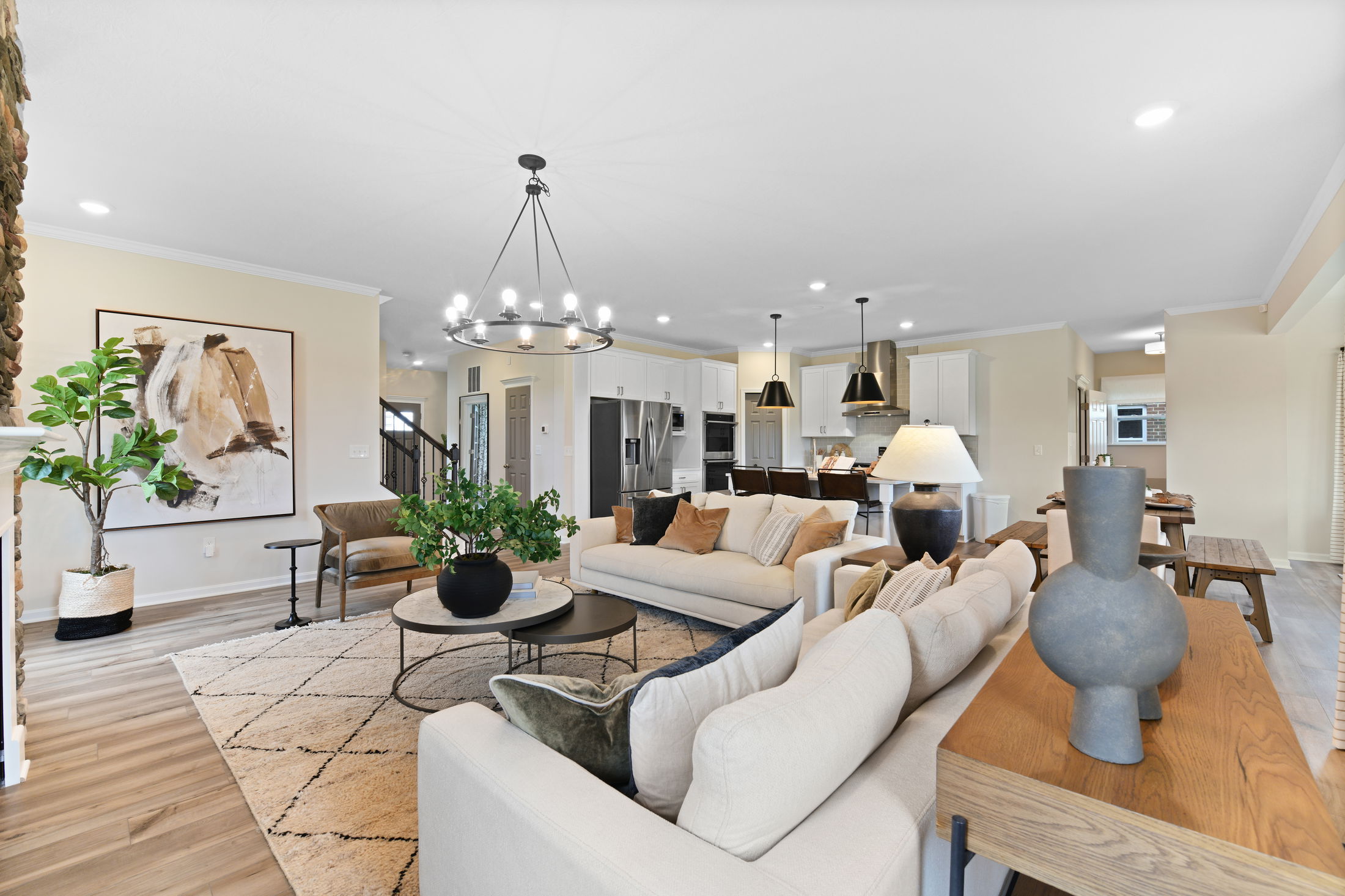 Open-concept living room with modern decor, featuring beige sofas, a large chandelier, and a view of the kitchen.