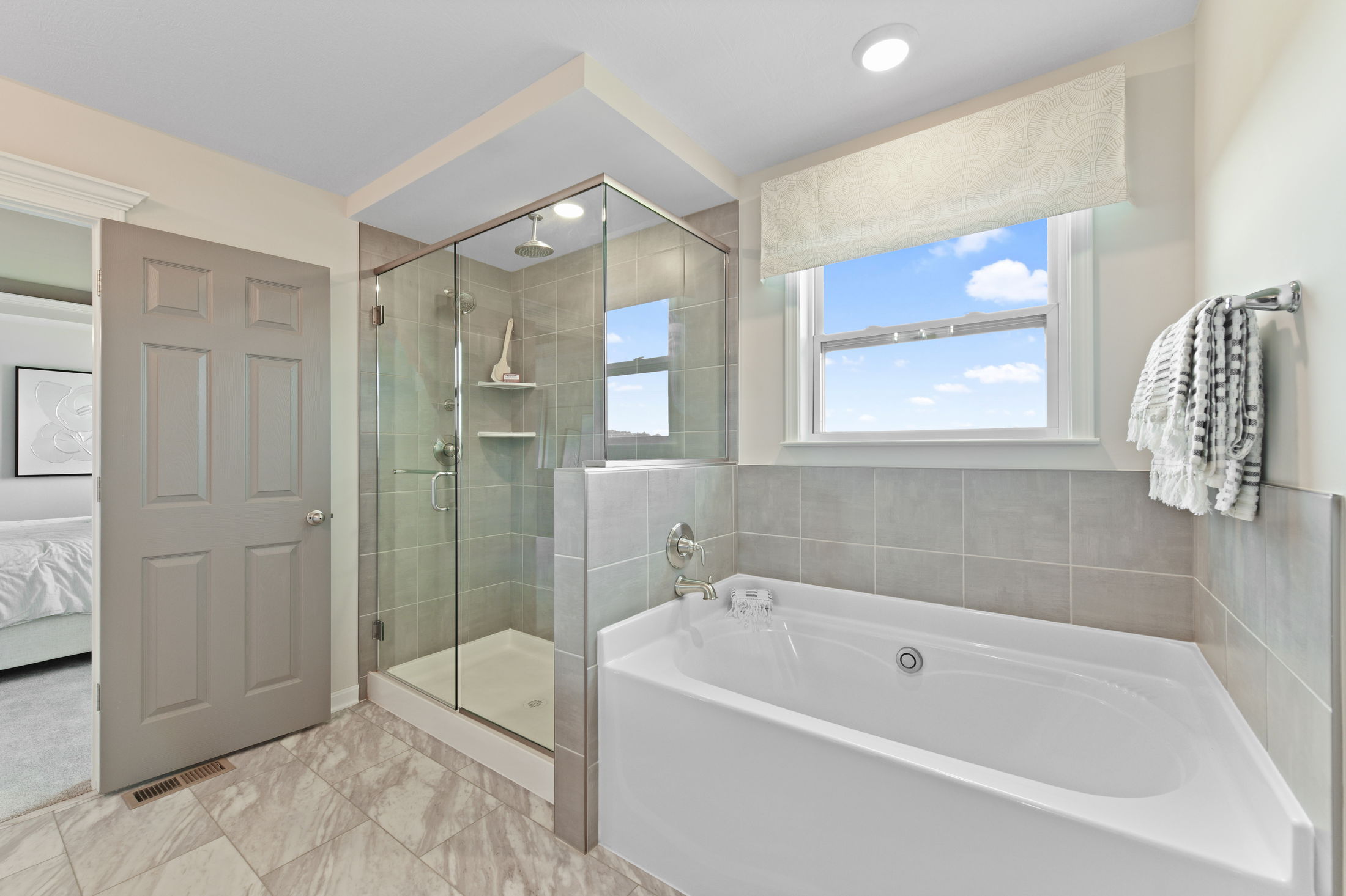Modern bathroom with a glass-enclosed shower and a large bathtub under a bright window.