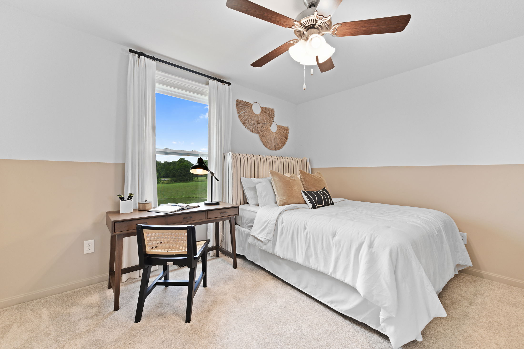 Modern bedroom with neutral tones featuring a cozy bed, wooden desk, and chair near a large window with scenic outdoor view.