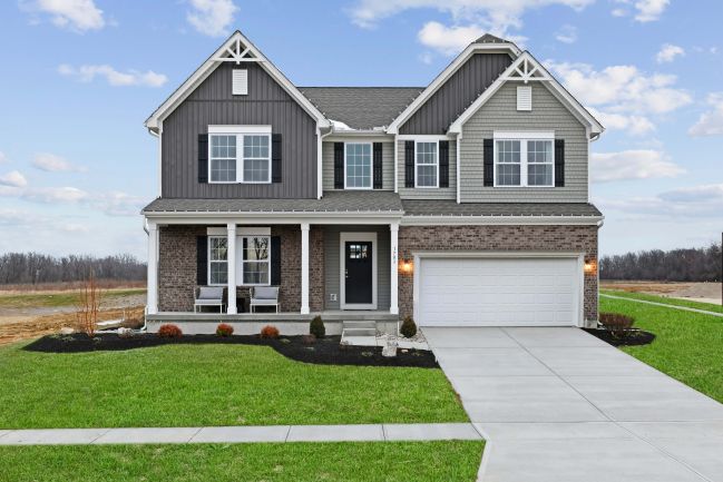 Two-story suburban house with gray siding, brick accents, and a double garage, set against a blue sky backdrop.