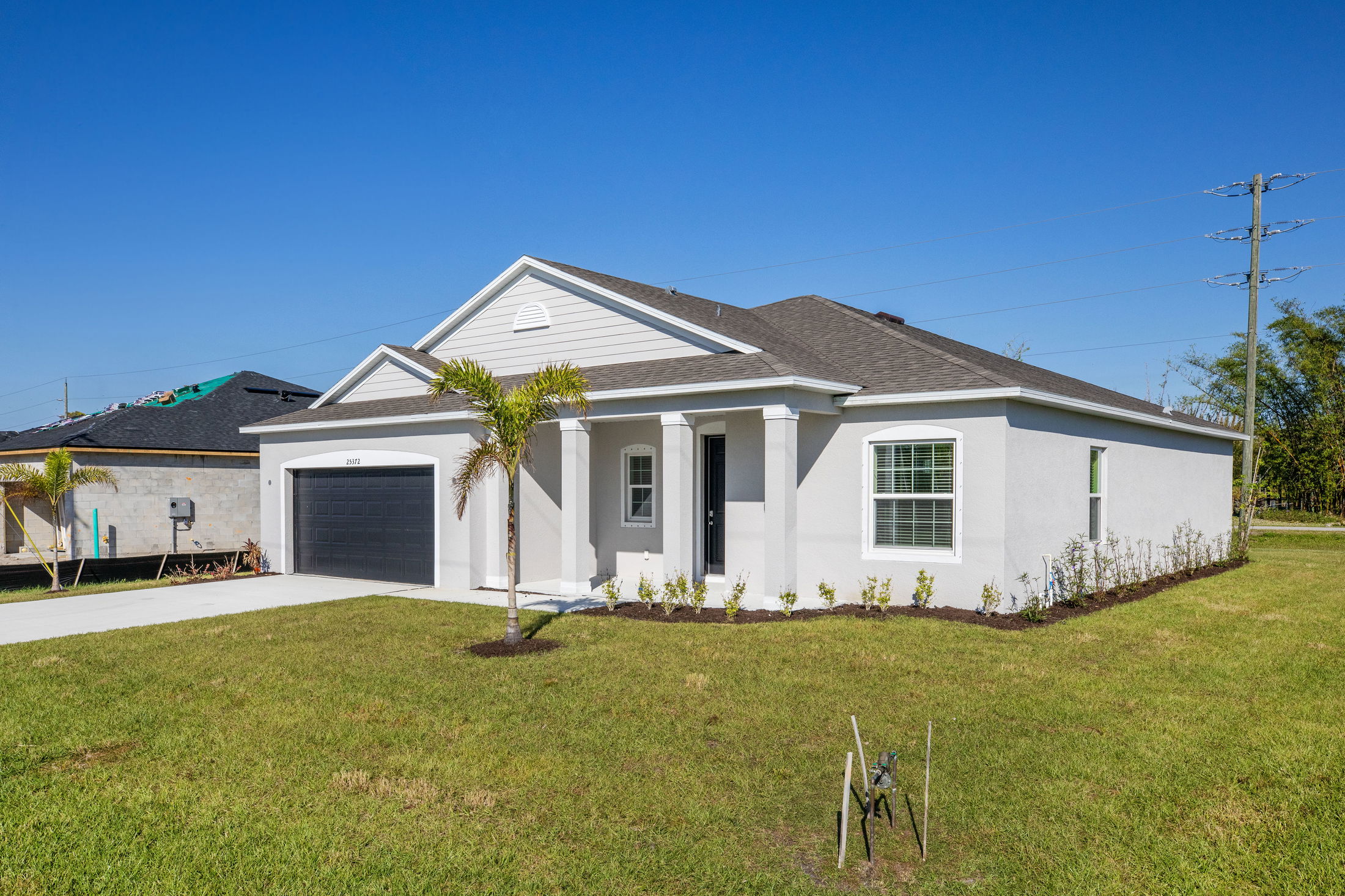 Newly built modern single-story house with a two-car garage, manicured lawn, and bright blue sky background.