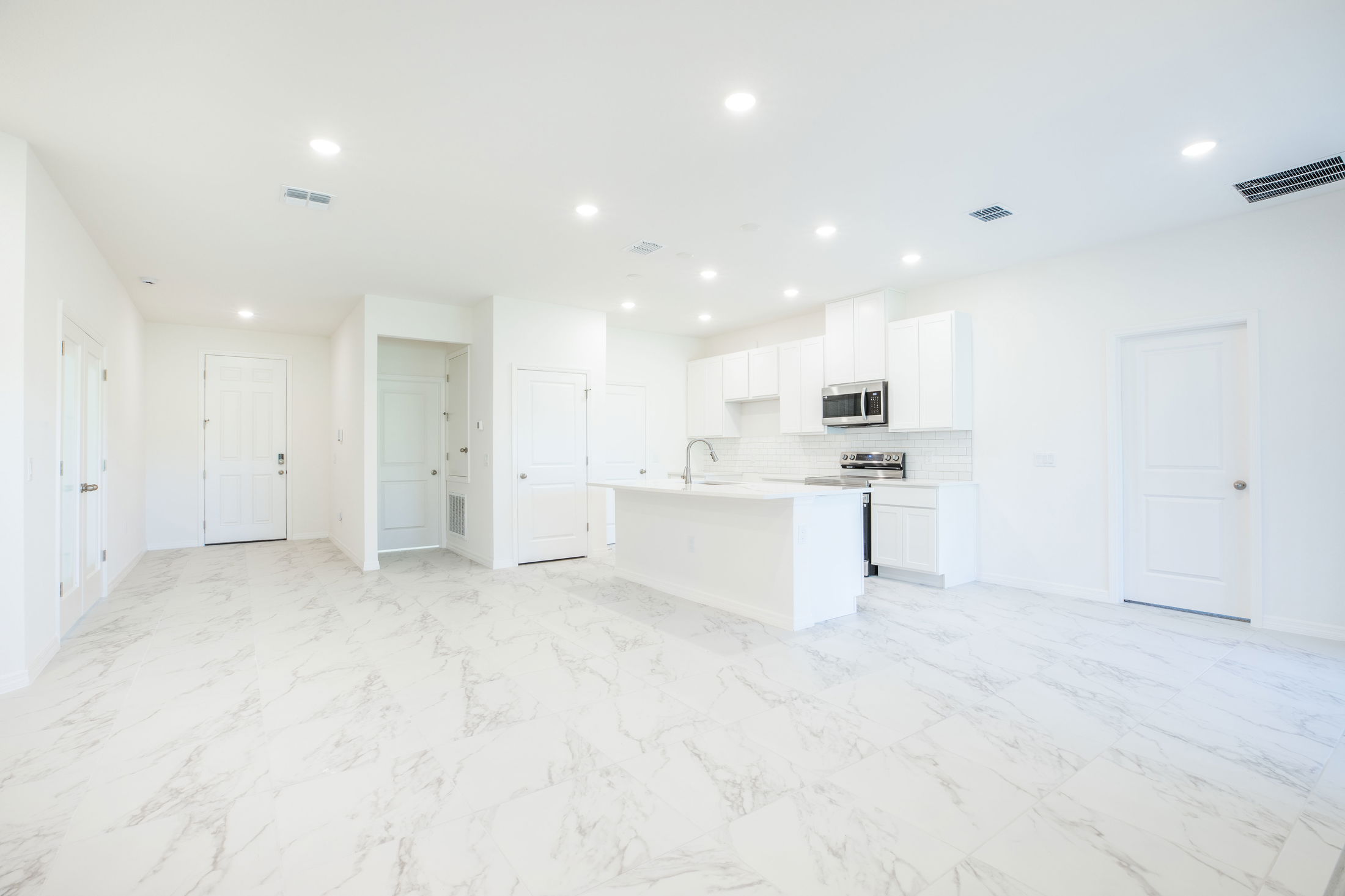 A bright, modern kitchen with white cabinetry, stainless steel appliances, and marble-patterned flooring.