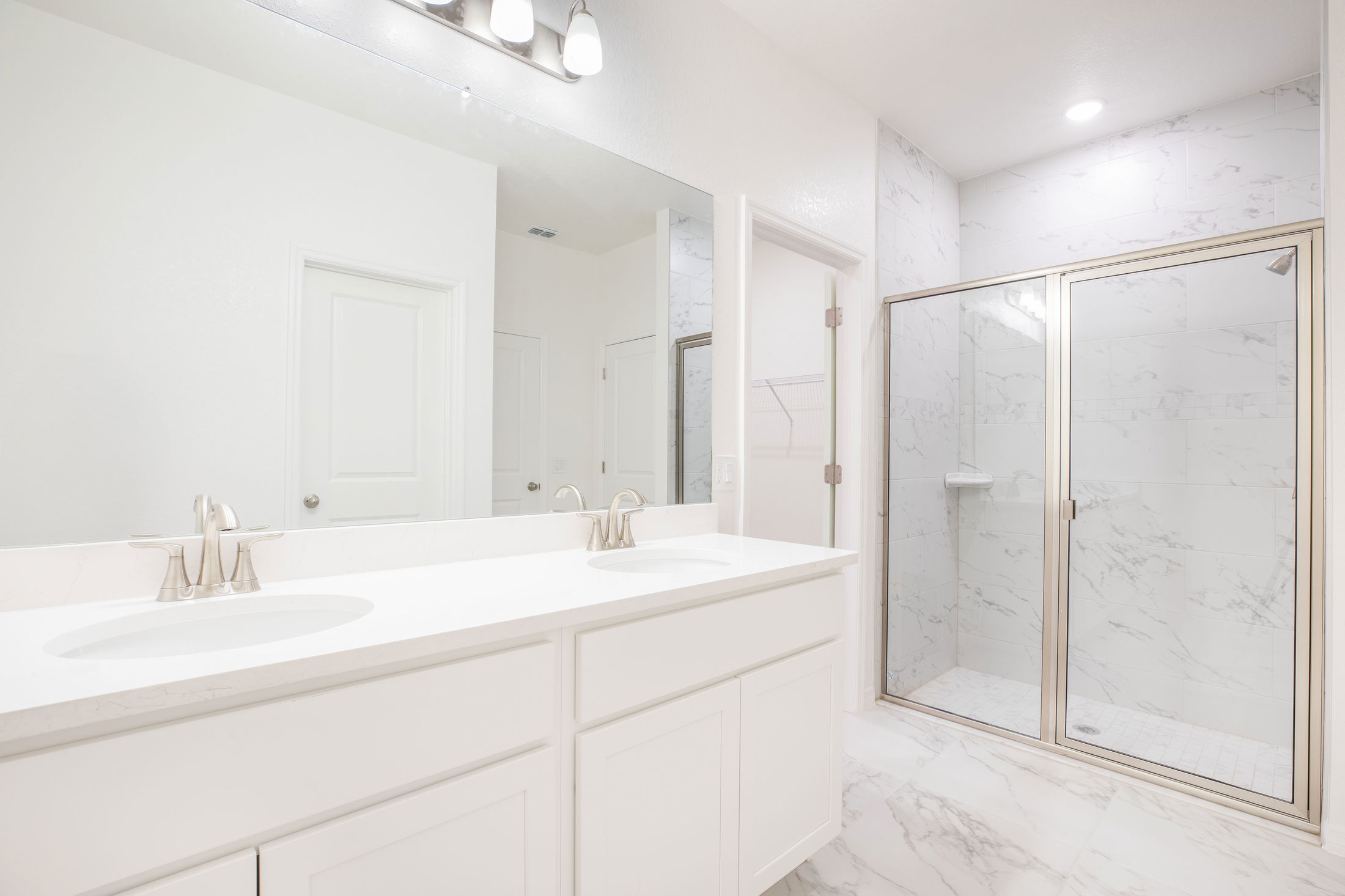 Bright and modern white bathroom featuring a double sink vanity with marble countertops and a spacious glass-enclosed shower.