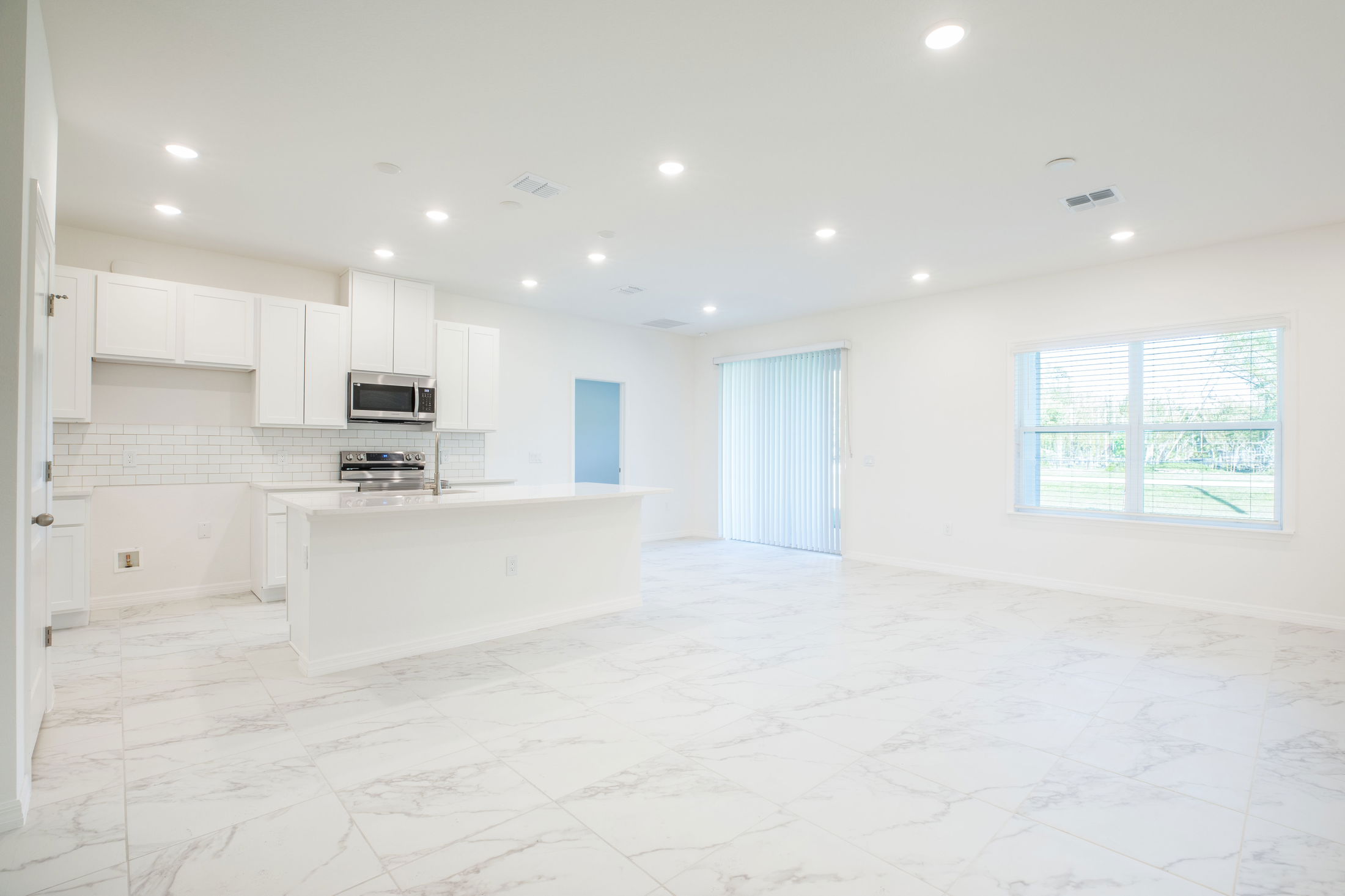 Bright and spacious open-concept kitchen and living area with white cabinets, marble tile flooring, and ample natural light.