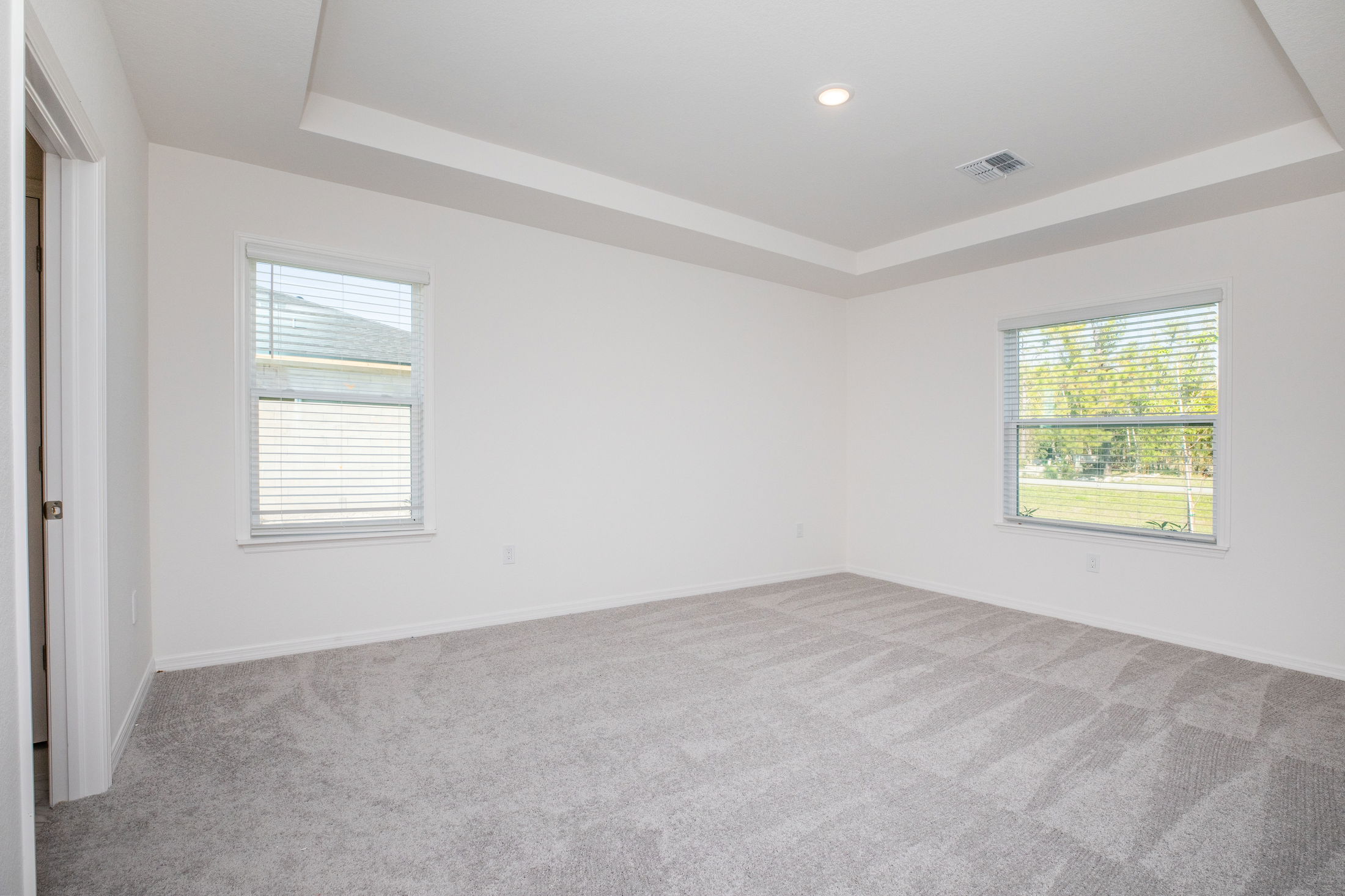 Empty room with clean gray carpet, white walls, and two windows with blinds.