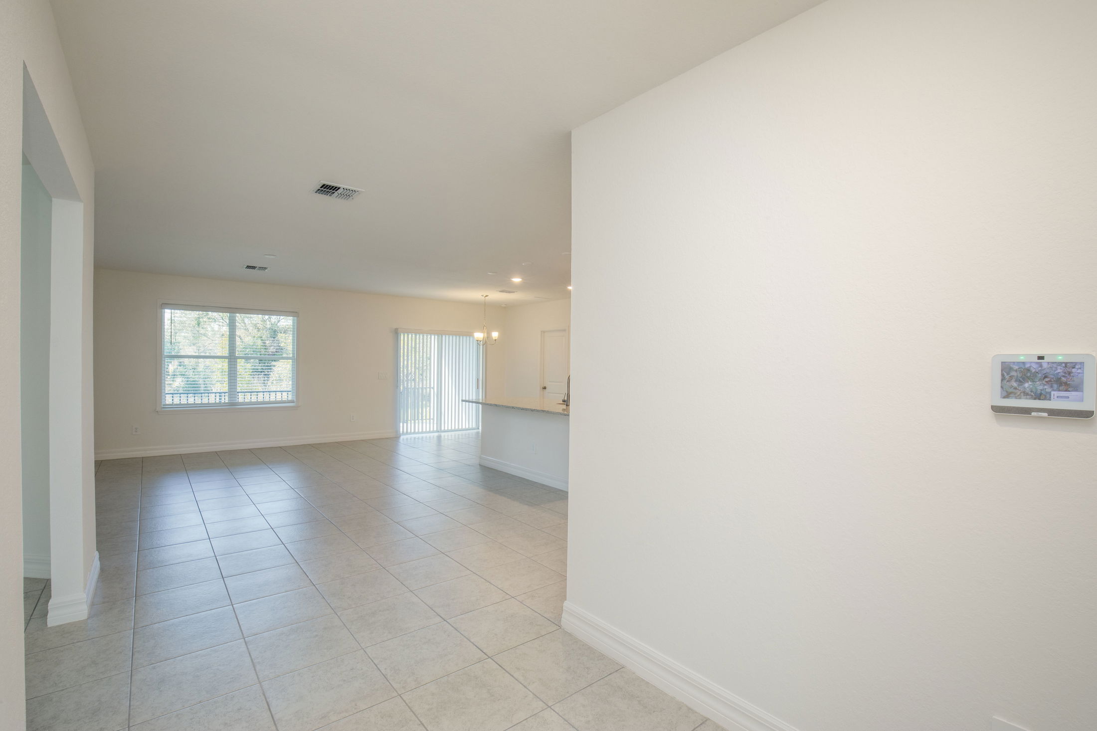 Modern empty living room interior with large windows and tiled flooring, featuring a view towards the kitchen area.