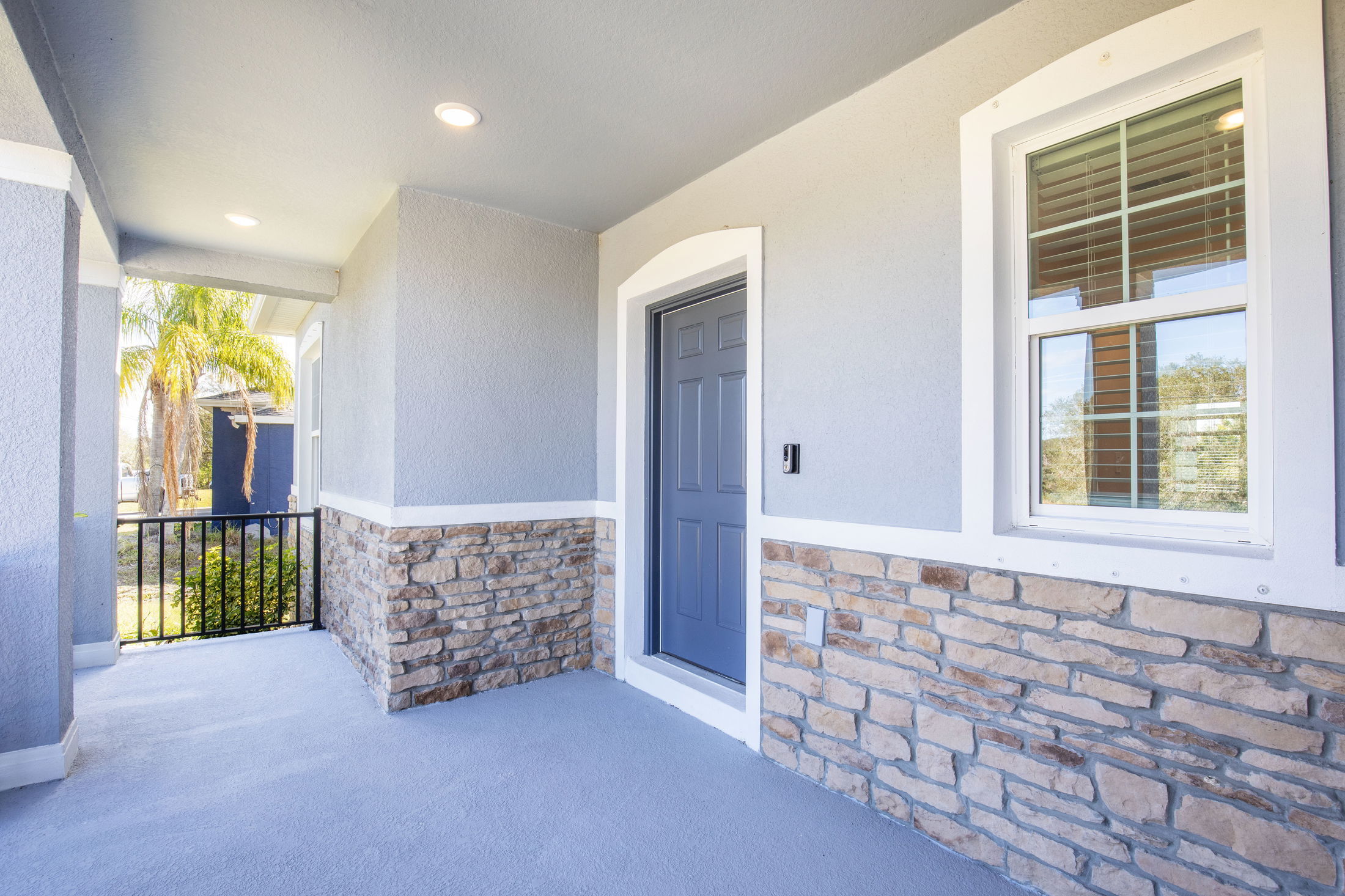 Modern home entrance with stone accent walls, blue door, and a window surrounded by white trim.
