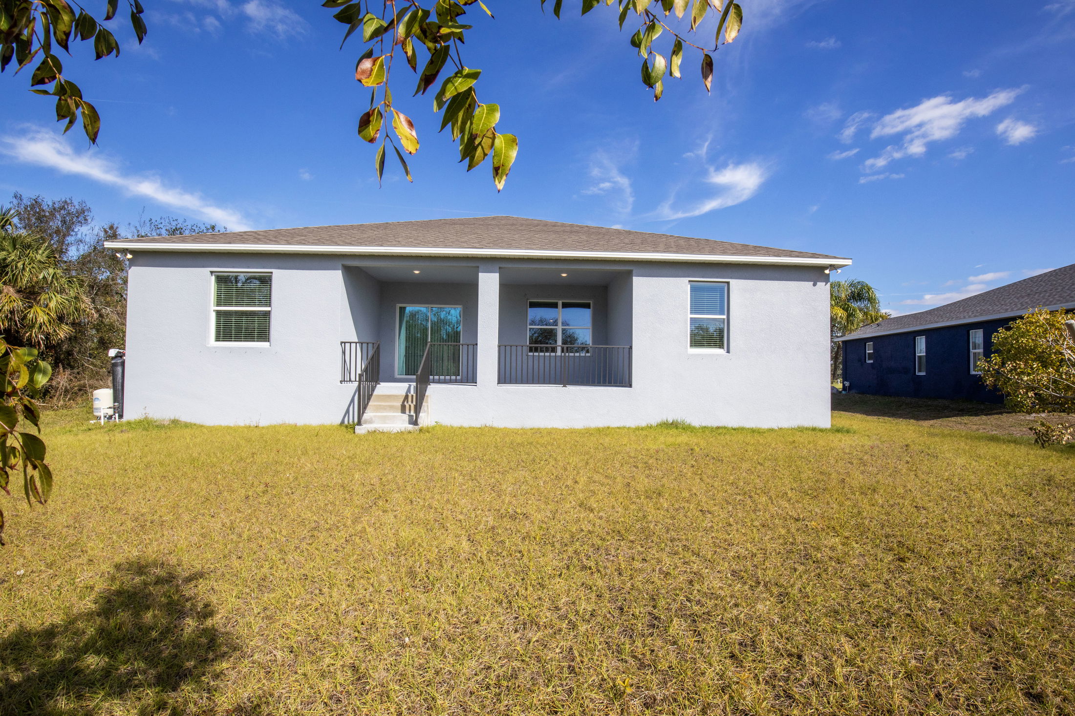 Front view of a single-story, modern gray house with a spacious lawn and clear blue sky.