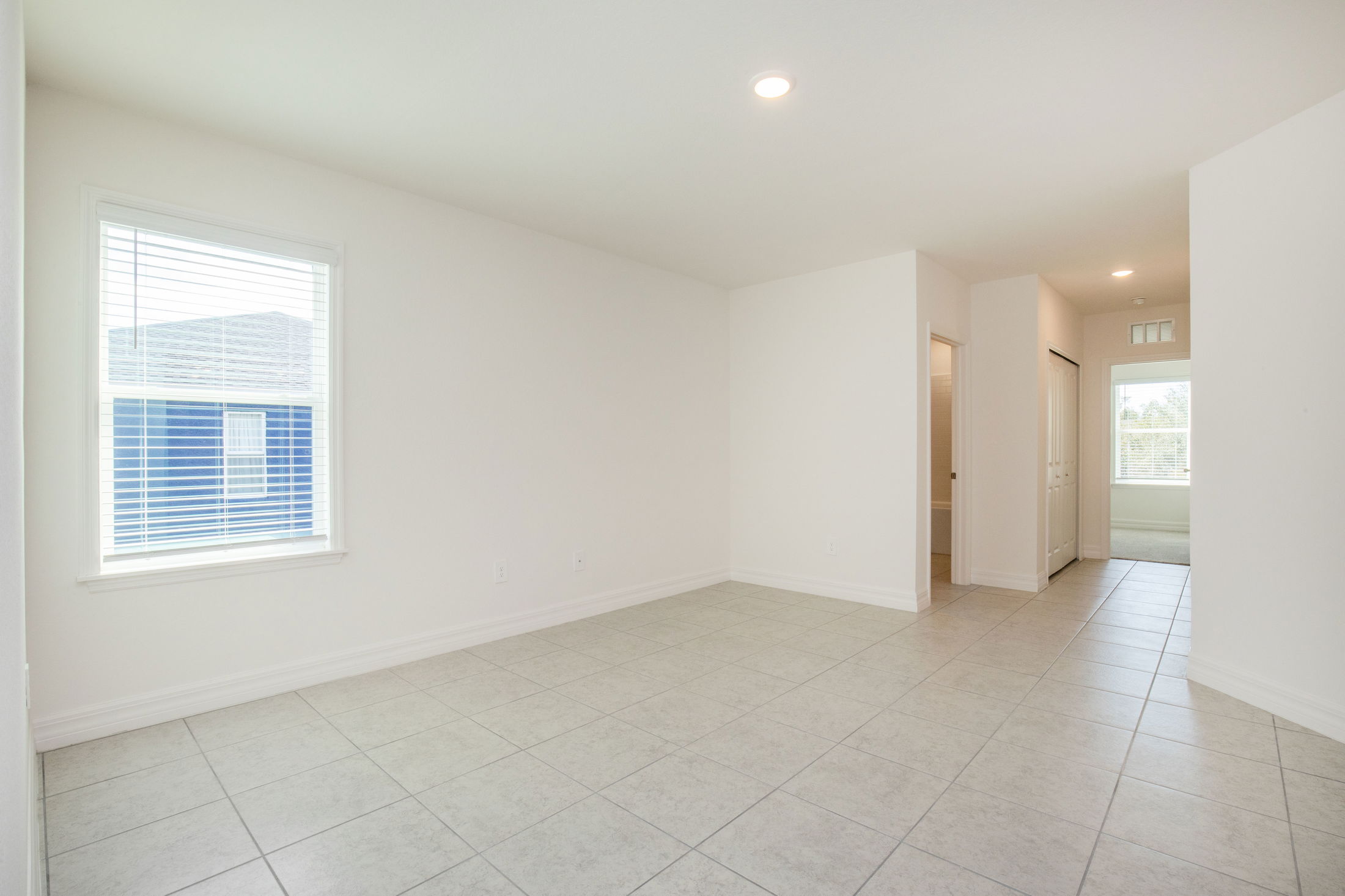 Empty, well-lit room with white walls, tiled floor, and a window.