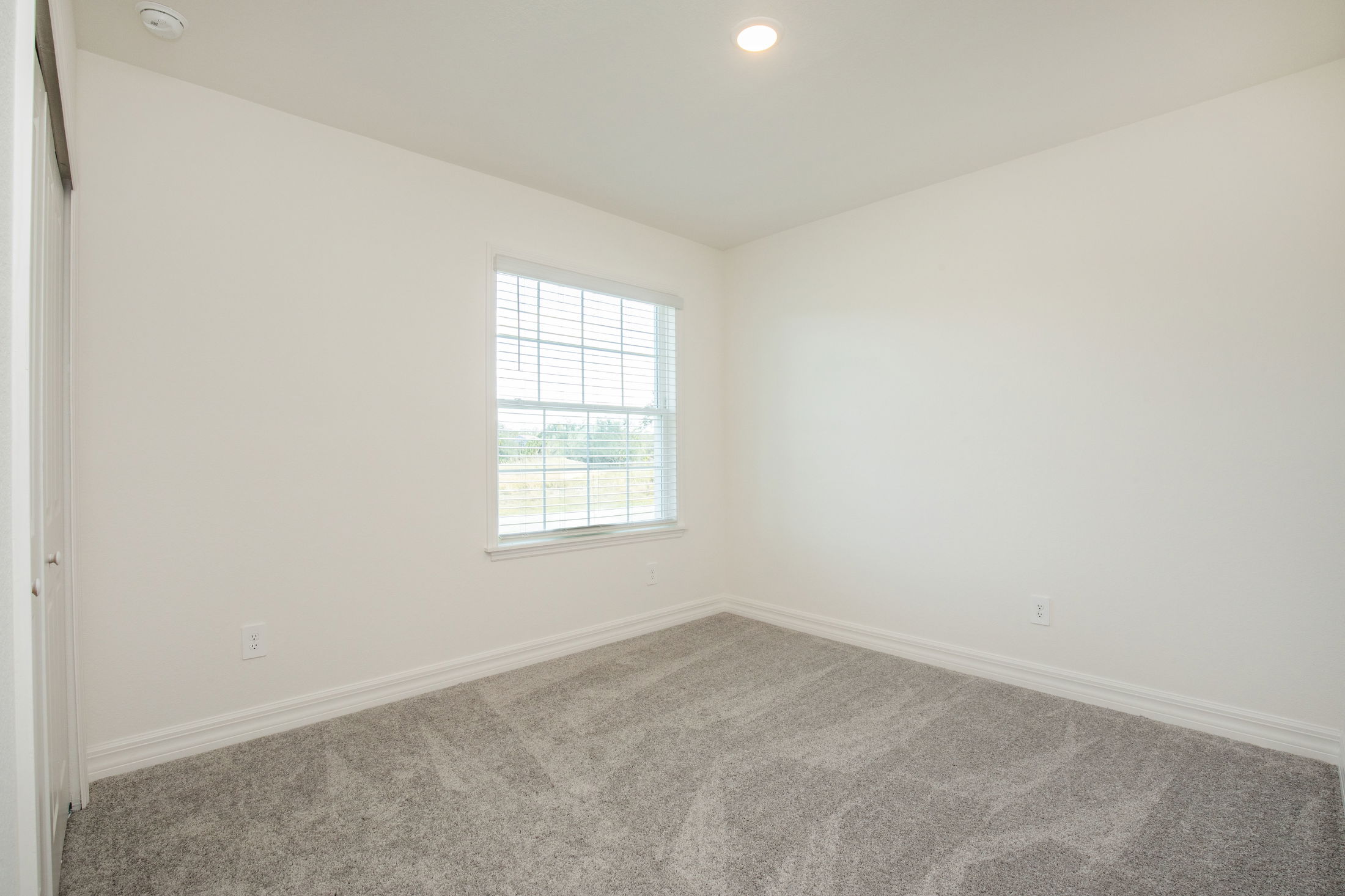 Empty bright room with white walls, large window, and gray carpet flooring.