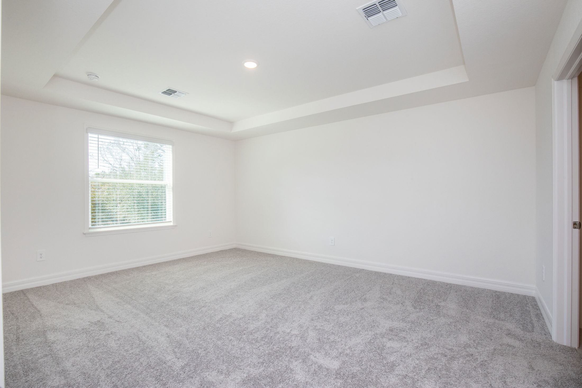 Empty room with white walls, plush gray carpet, recessed lighting, and a window bringing in natural light.