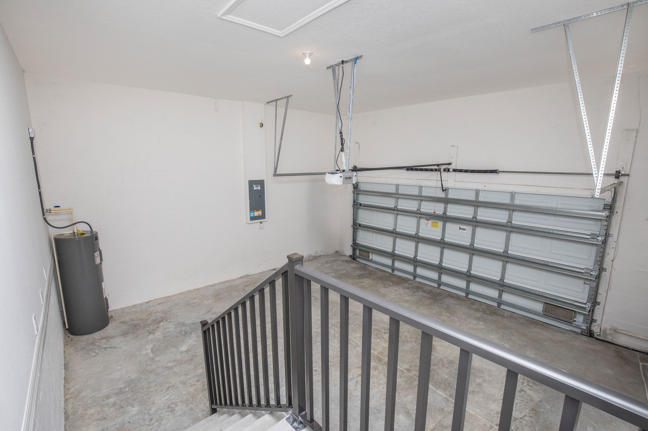 Empty residential garage interior with concrete floor, metal railing, closed garage door, and water heater.