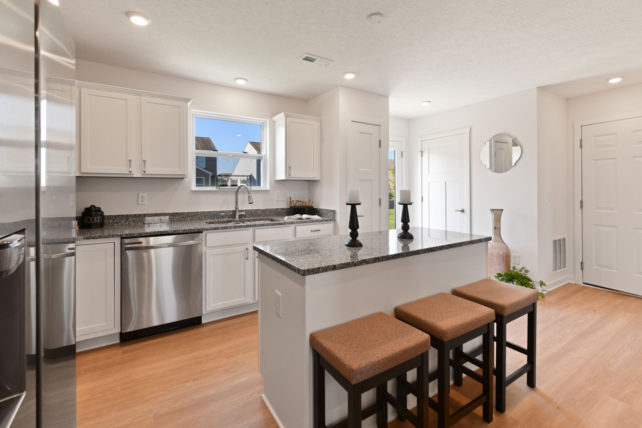 Modern kitchen with white cabinetry, granite countertops, stainless steel appliances, and a central island with bar stools.