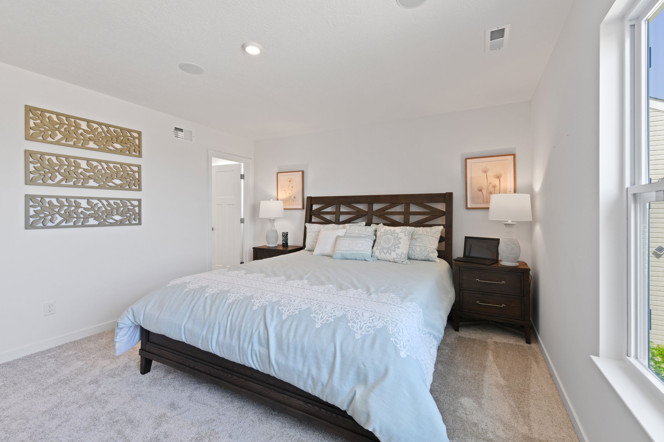 Modern bedroom with light blue bedding, wooden headboard, and elegant decor elements on white walls.