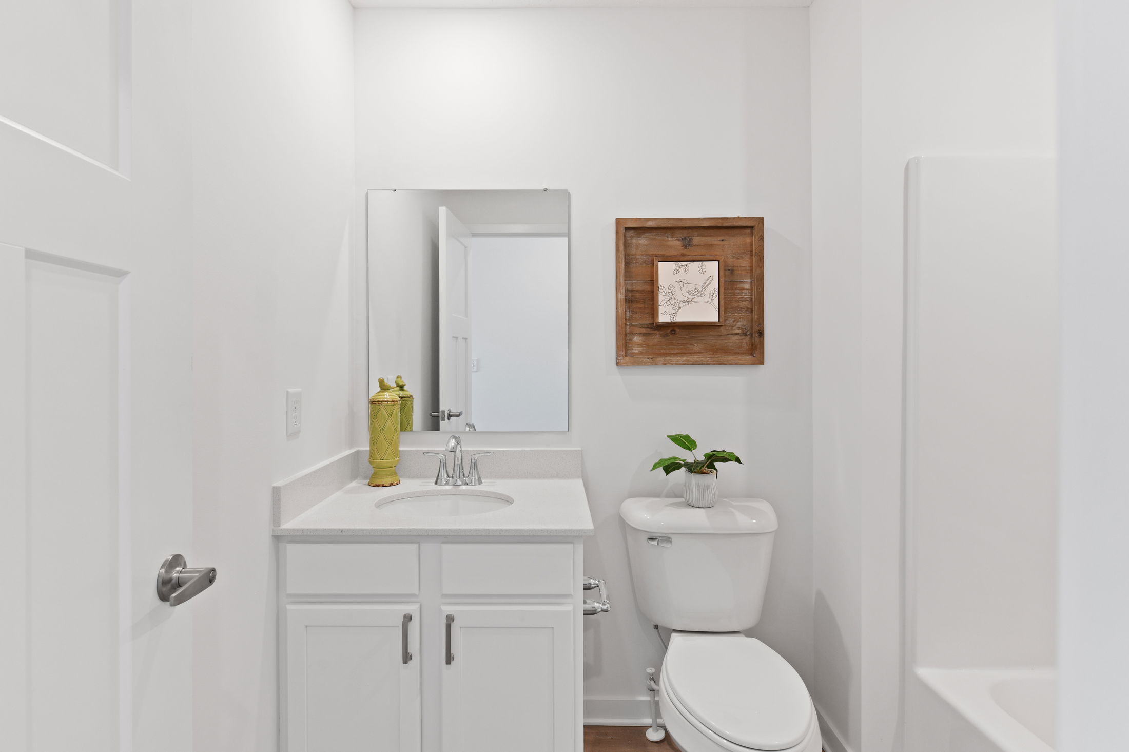Small modern bathroom with white cabinets, a toilet, decorative wall art, and a plant on the tank.