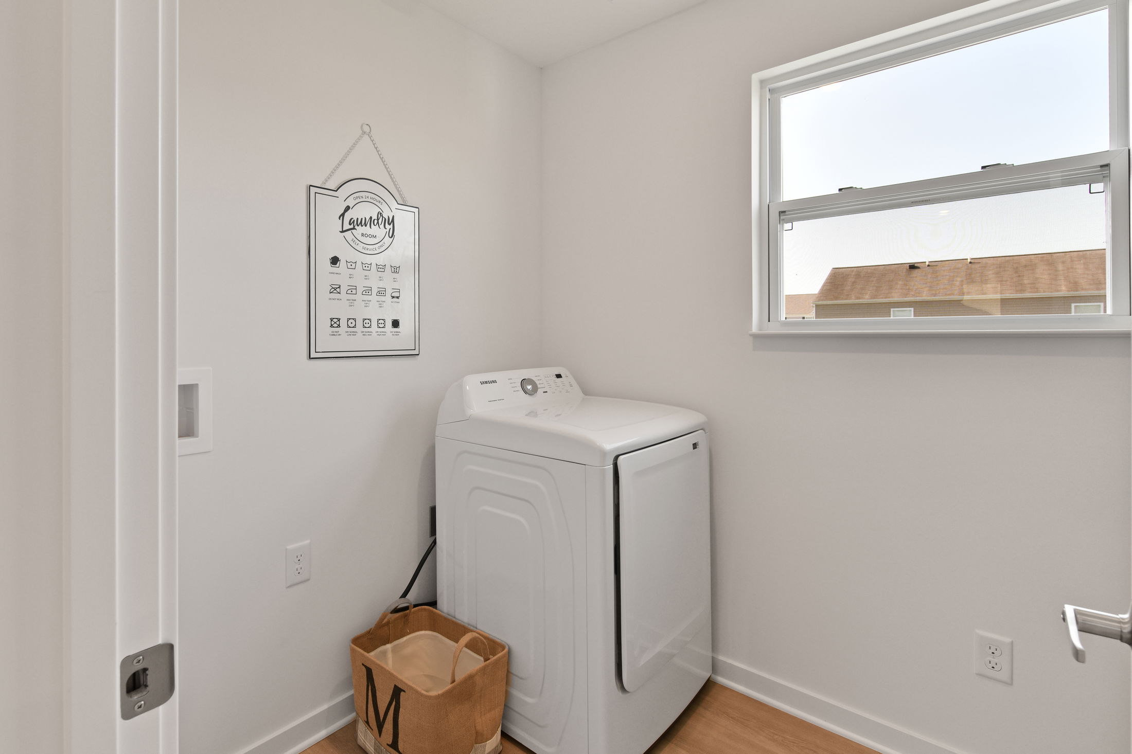 Bright laundry room featuring a modern white washing machine, a laundry guide wall decoration, and a nearby basket under a window.