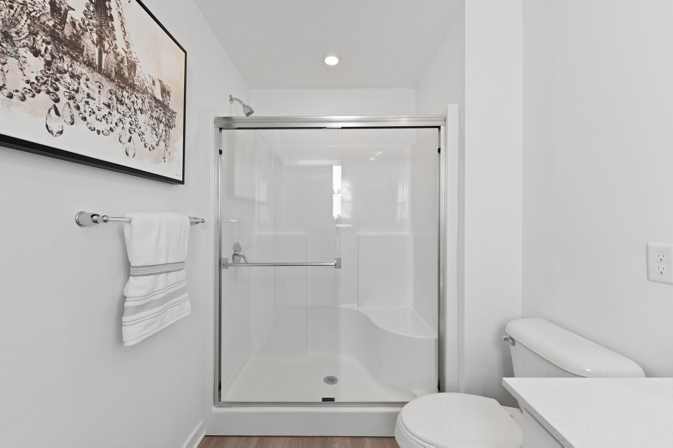 Minimalist white bathroom featuring a glass shower enclosure, modern fixtures, and wall art.