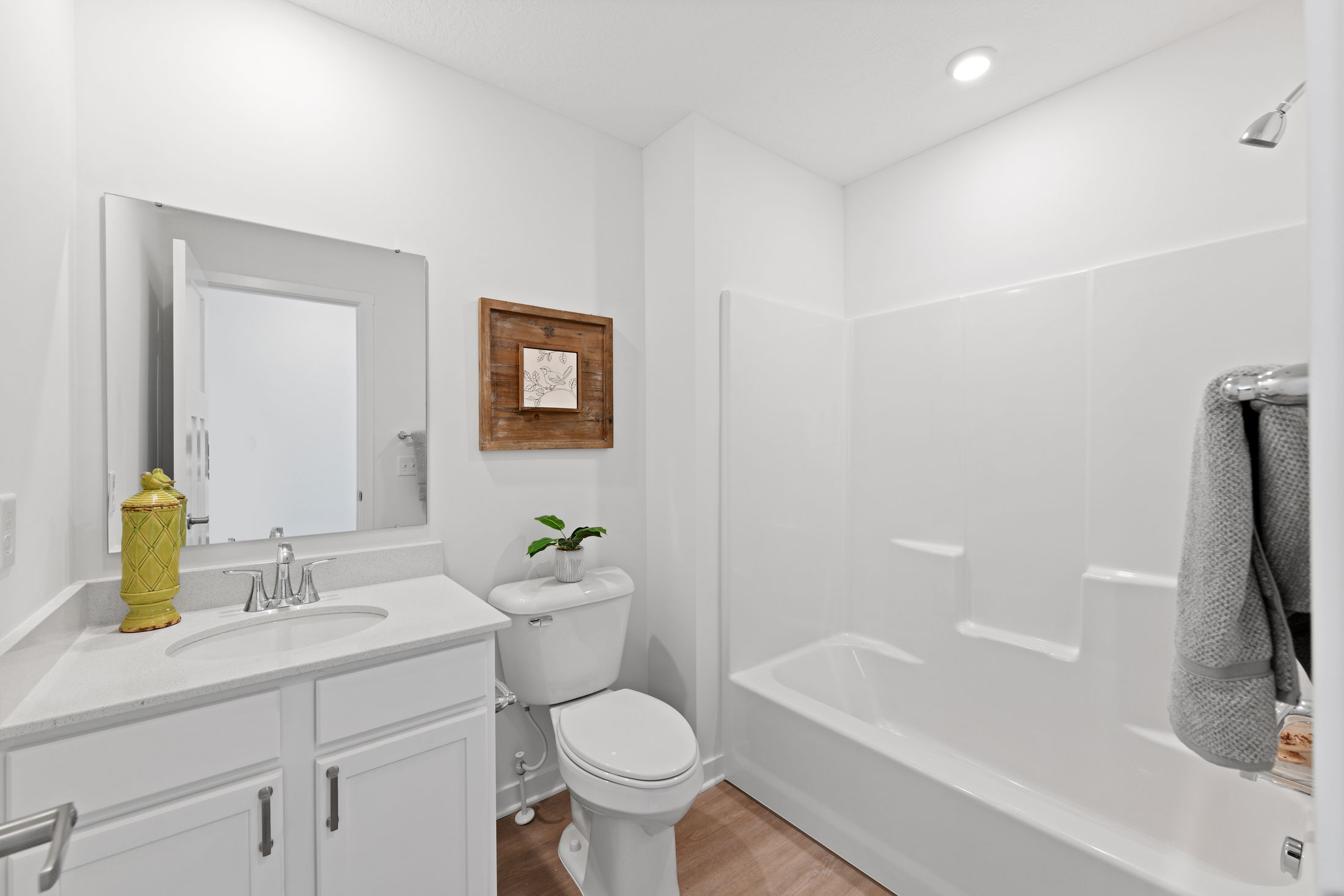 Modern white bathroom with sleek vanity, shower-tub combo, decorative wall art, and potted plant for a minimalist look.