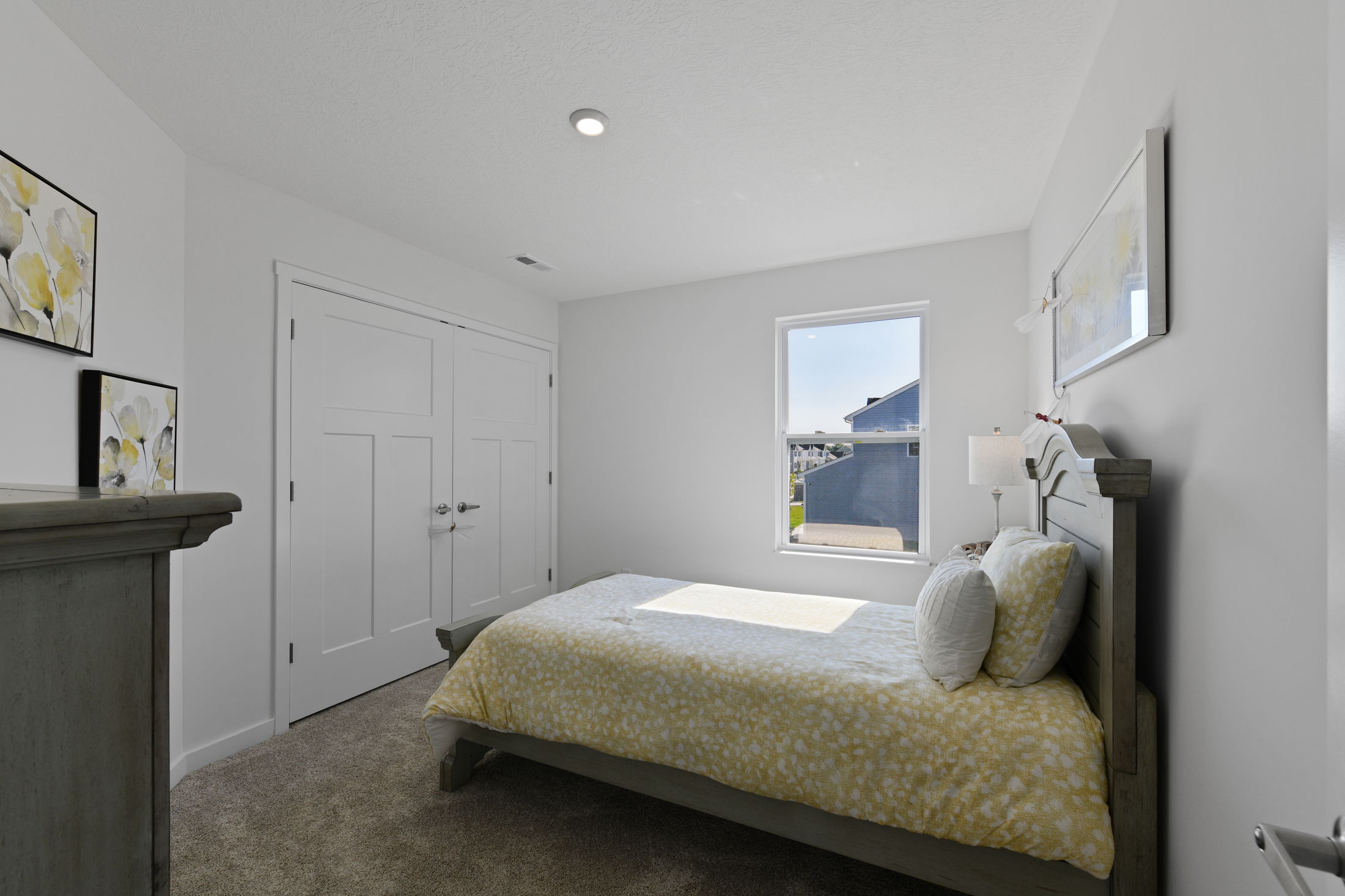 Modern bedroom with a yellow patterned bedding set, white walls, and natural light streaming through a window.