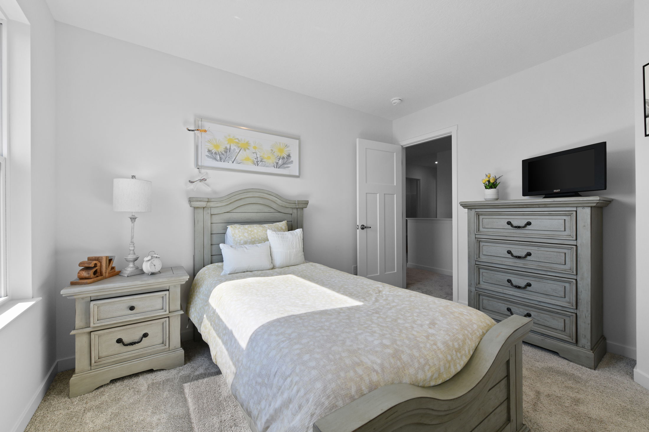 Cozy, modern bedroom featuring a single bed with a light wood headboard, matching bedside table, dresser, and a mounted flat-screen TV against a soft grey wall.