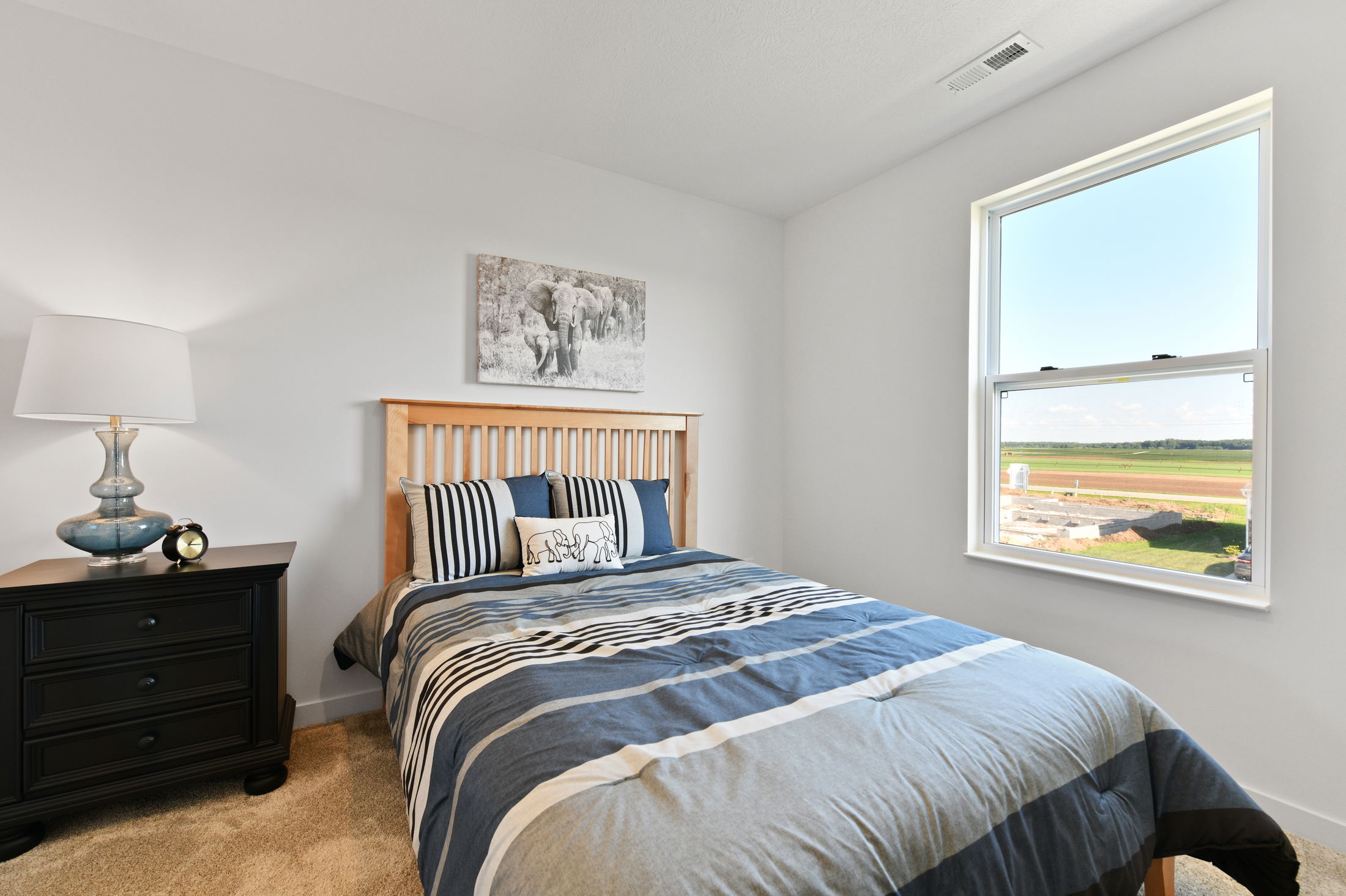 A cozy, modern bedroom featuring a twin-sized bed with blue striped bedding, wooden headboard, black nightstand with lamp, and a scenic window view.