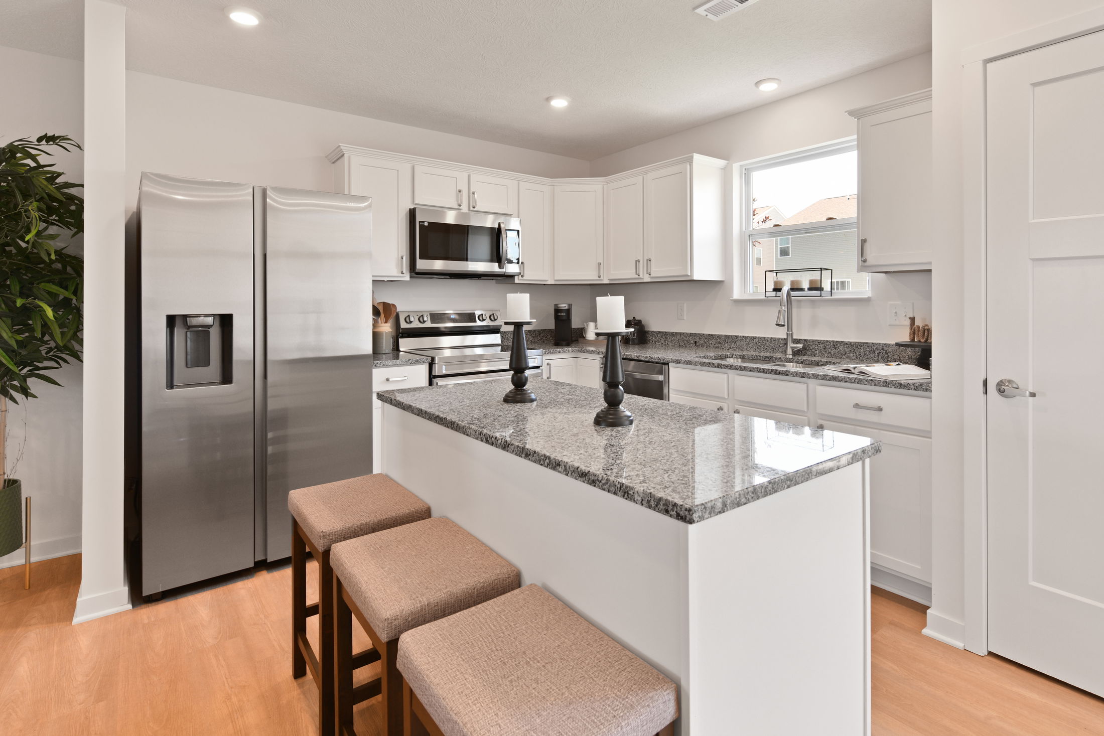 Modern kitchen with white cabinets, stainless steel appliances, granite countertops, and beige cushioned bar stools.