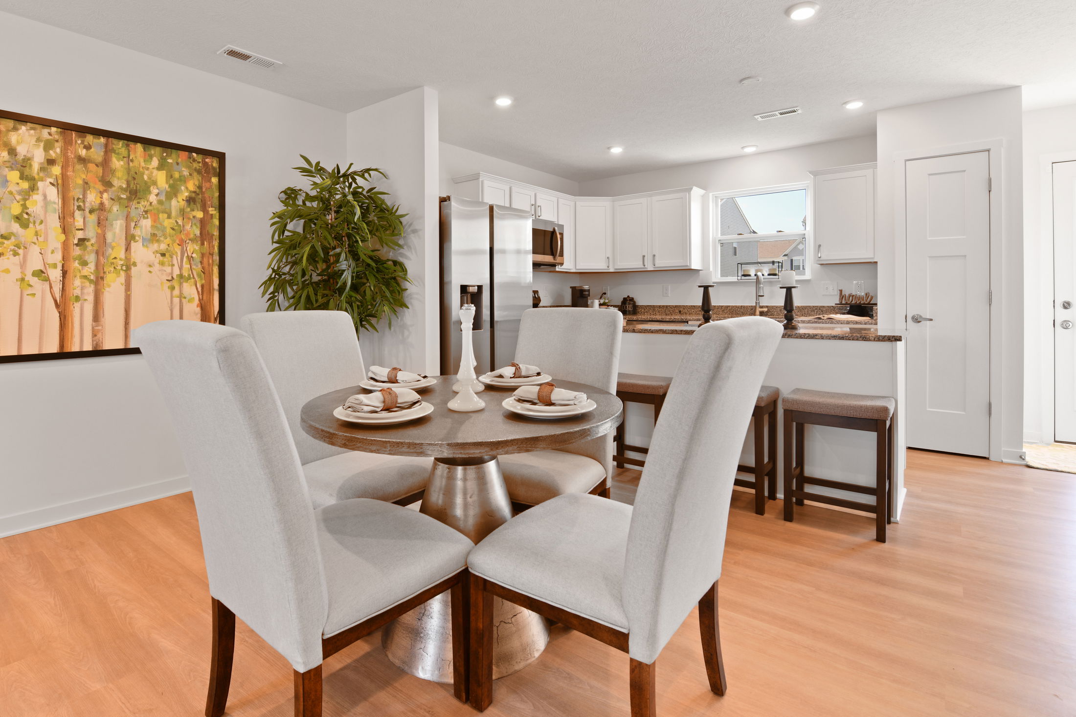 Bright, modern kitchen and dining area with wood floor, round table set for four, white cabinets, and artwork on the wall.
