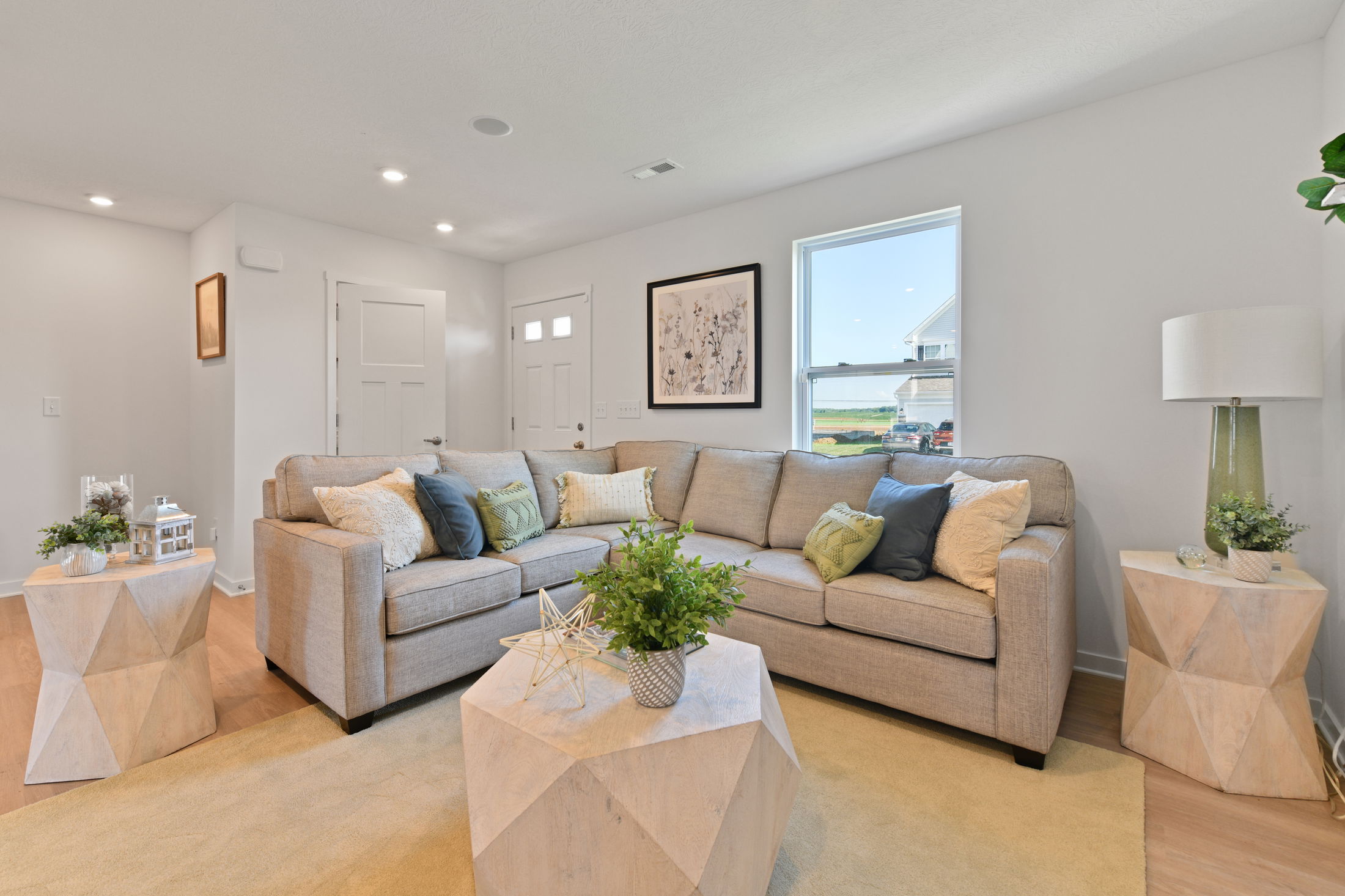 Modern living room with a beige sectional sofa, geometric wooden tables, and decorative plants.