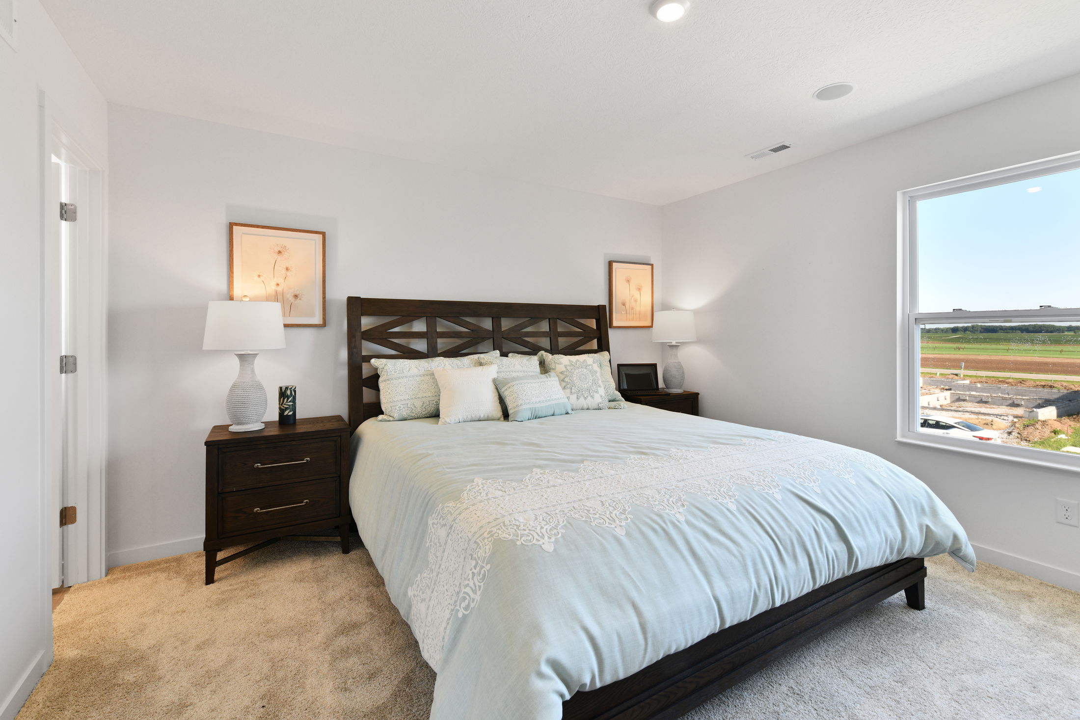 Modern bedroom with a cozy light blue bedding set, dark wooden bed frame, matching nightstands, and natural light from a large window.