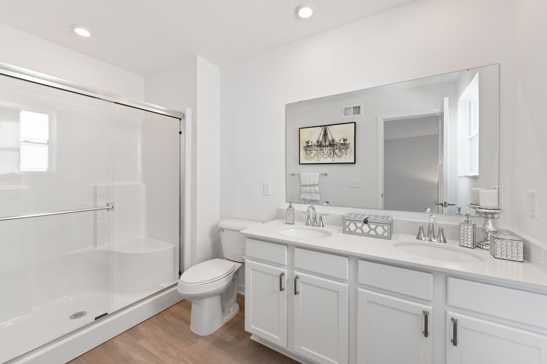 Modern white bathroom featuring a double vanity sink, glass-enclosed shower, and decorative elements for a clean, elegant look.