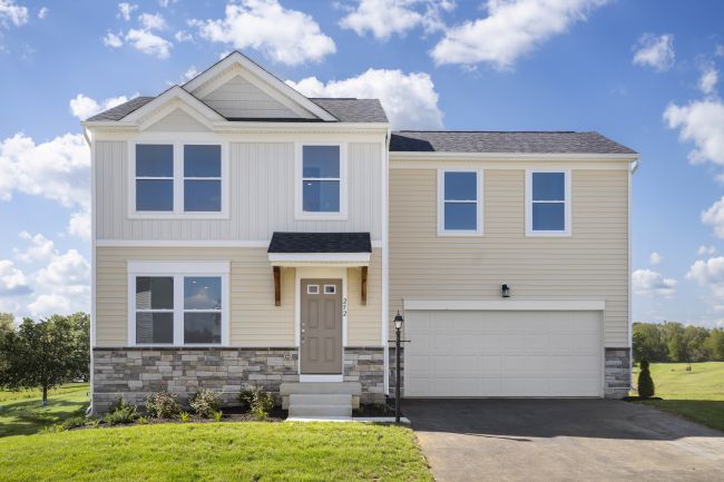 Two-story suburban home with a modern design, featuring beige siding, stone accents, and a spacious driveway under a clear blue sky.