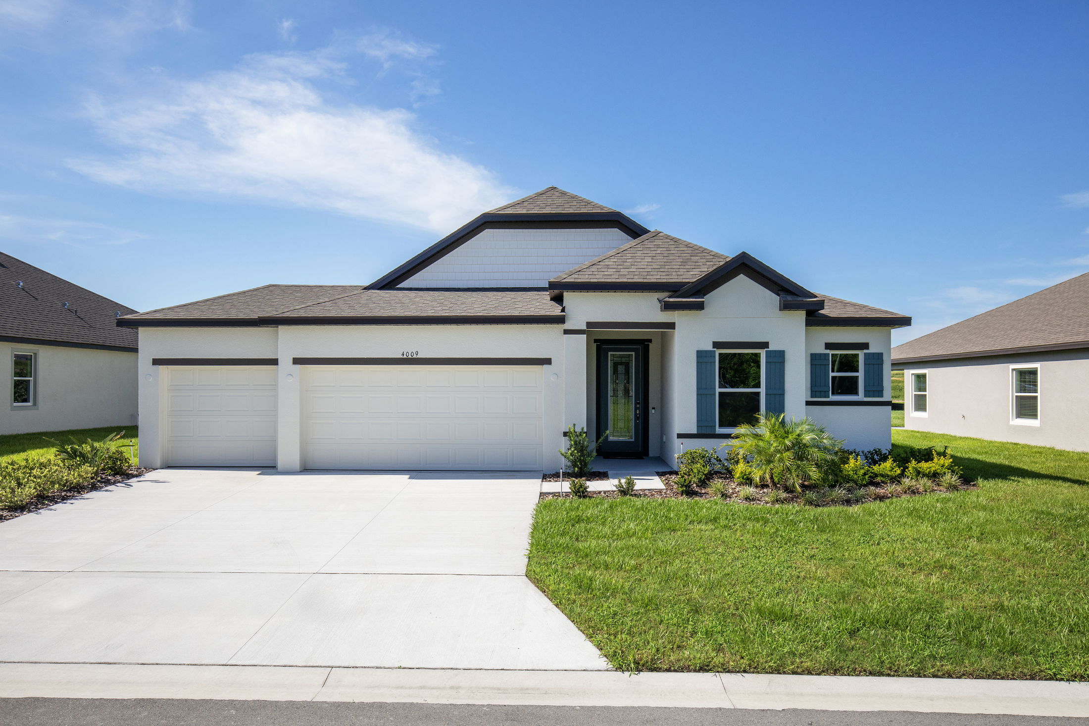 Modern single-story suburban home with a three-car garage and landscaped front yard under a clear blue sky.
