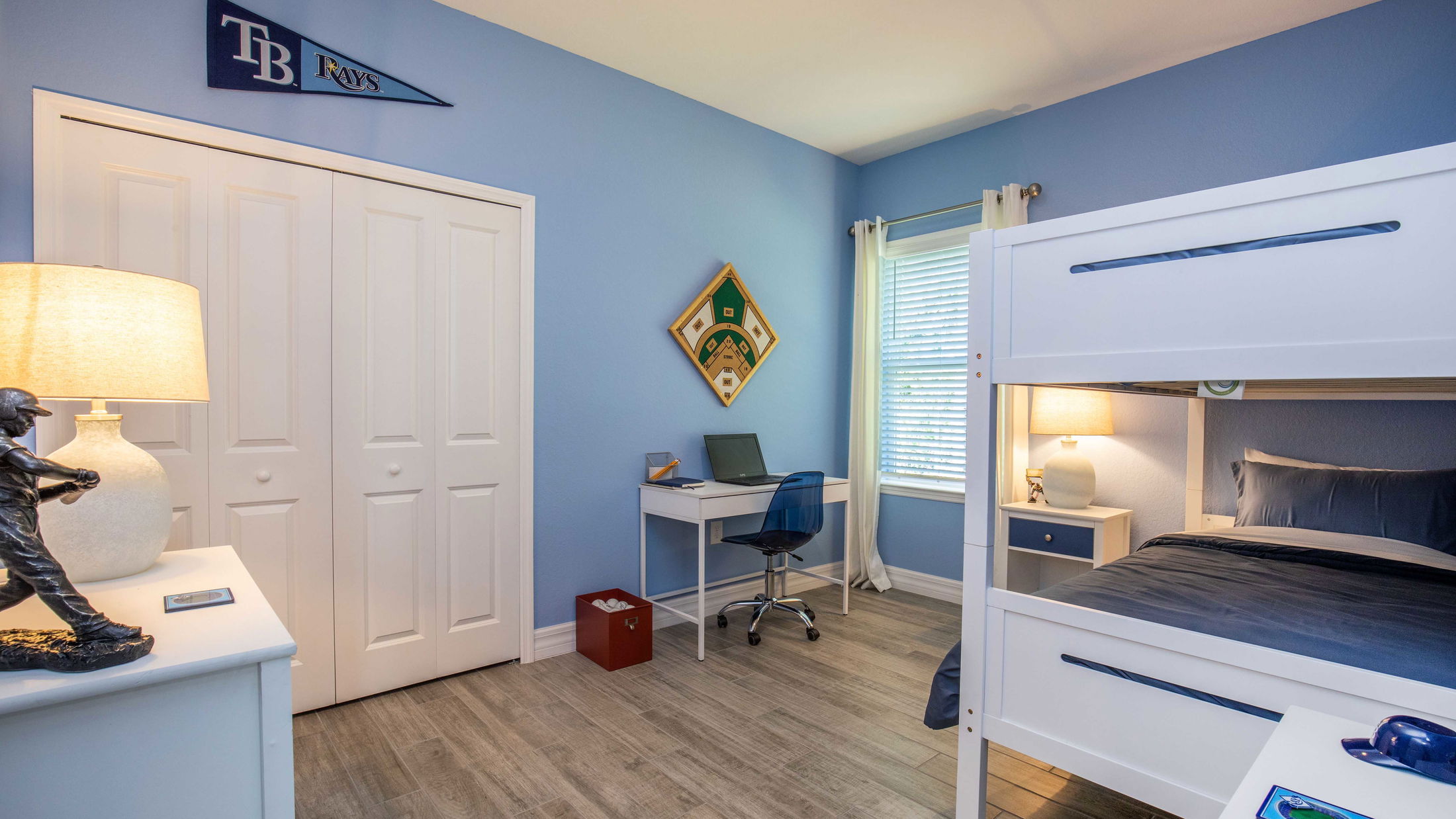 A modern blue-themed bedroom with a bunk bed, study desk, and sports decor featuring Tampa Bay Rays memorabilia.