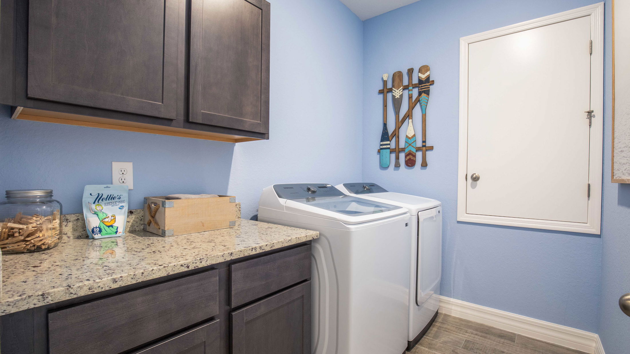 Modern laundry room with blue walls, featuring a granite countertop, cabinets, and Samsung washer and dryer.