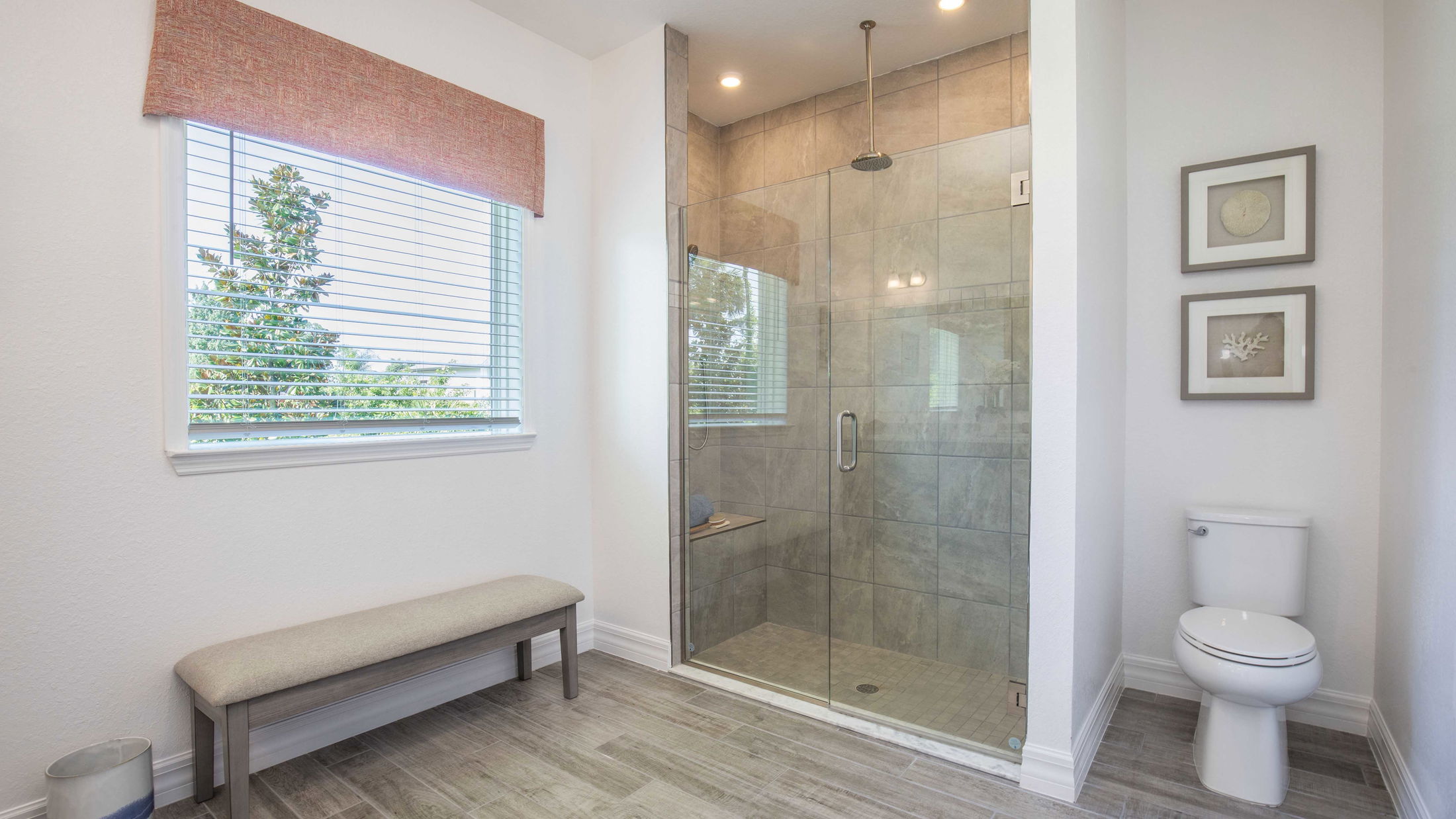 Modern bathroom with glass-enclosed shower, toilet, and natural light from a window with blinds.
